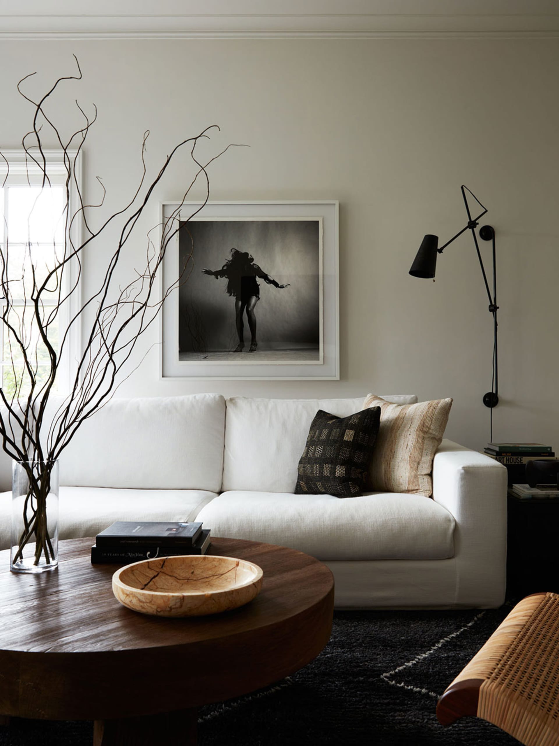 A minimalist living room featuring a white couch, black walls, and various decor items including a vase with long branches, a