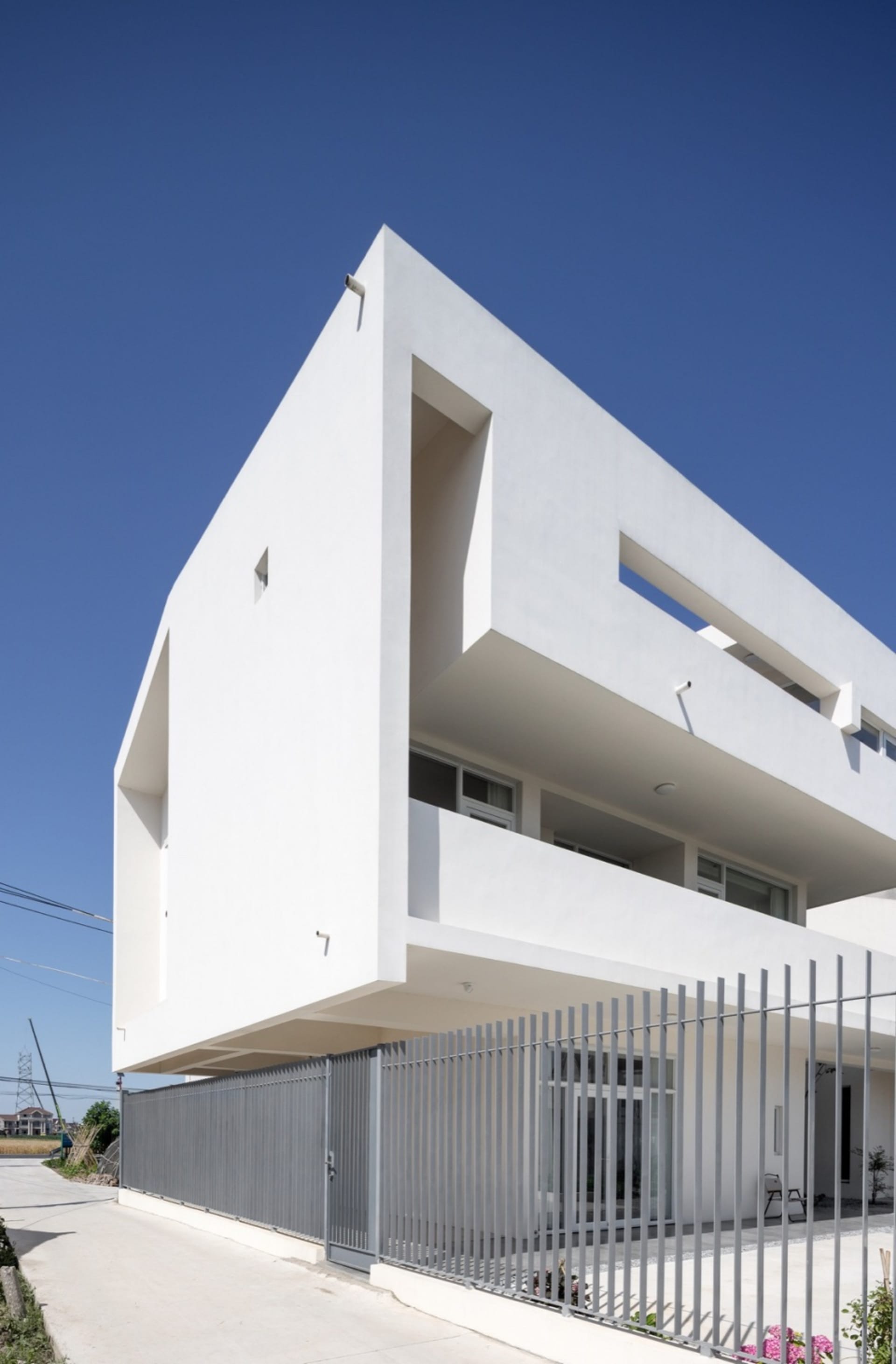 A modern building with a white concrete exterior, featuring a minimalistic design with large windows and a flat roof.