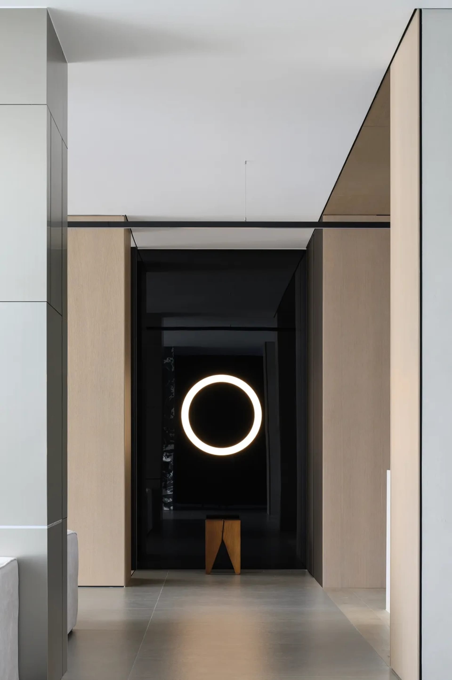 Modern minimalist entrance featuring a black glass wall, circular light fixture, and wood bench.