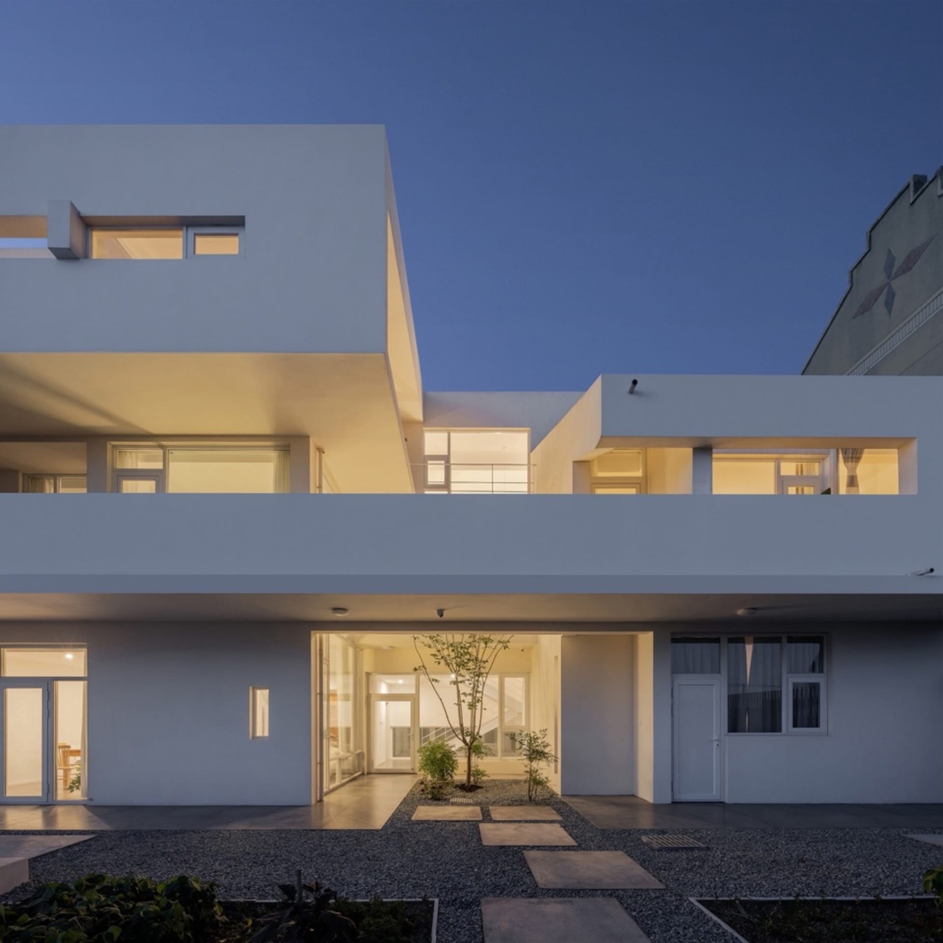Modern residential building with concrete exterior and illuminated windows during dusk.