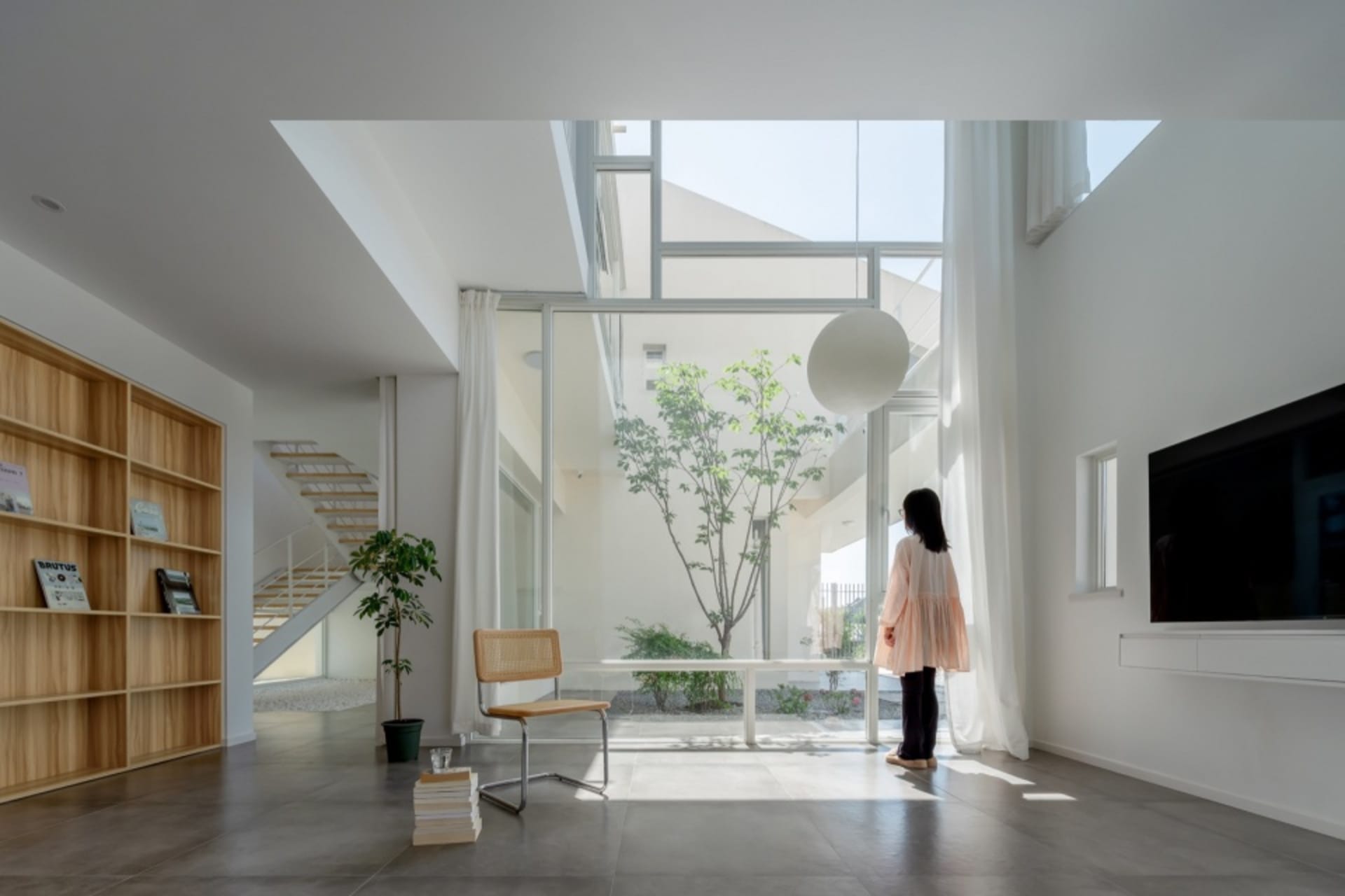 A minimalist living room with concrete flooring, large glass windows, and white furnishings.