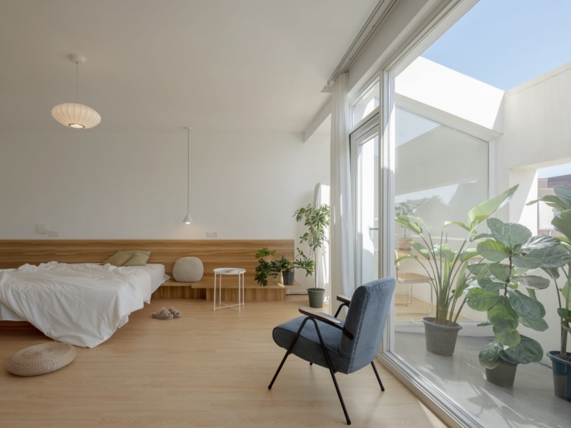 A minimalist modern bedroom featuring a wood floor, white bed, and large window.