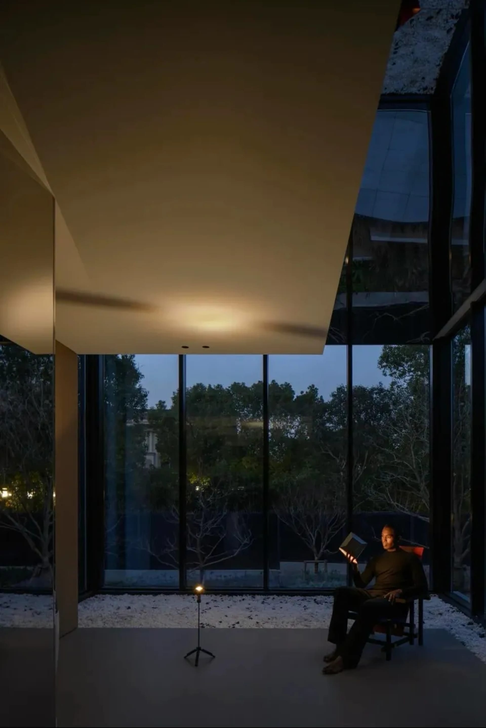 A modern interior design featuring a glass window with a person reading a book at dusk.
