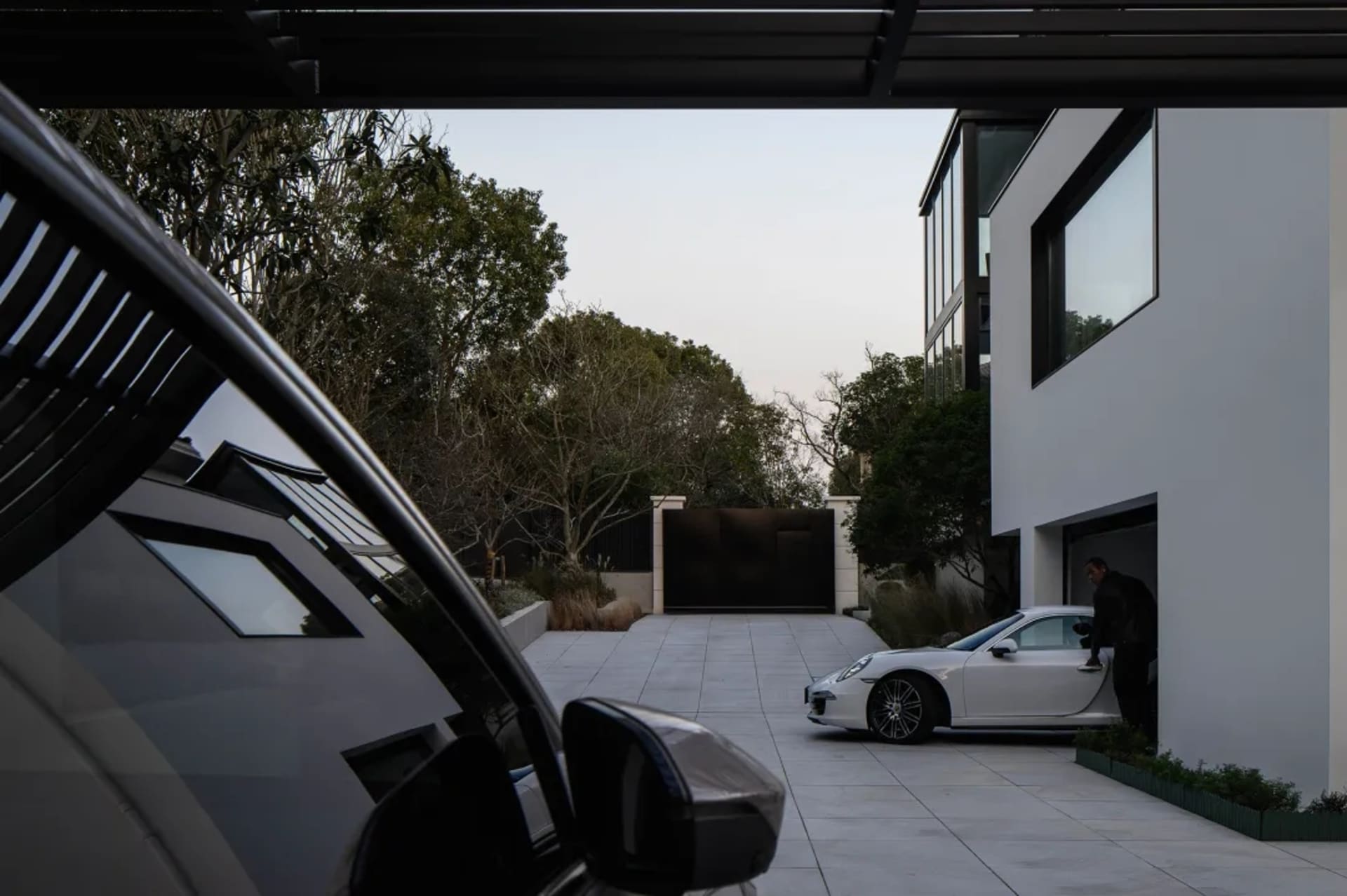 A modern garage with a white sports car parked inside. The exterior features large windows and doors, and the surrounding are