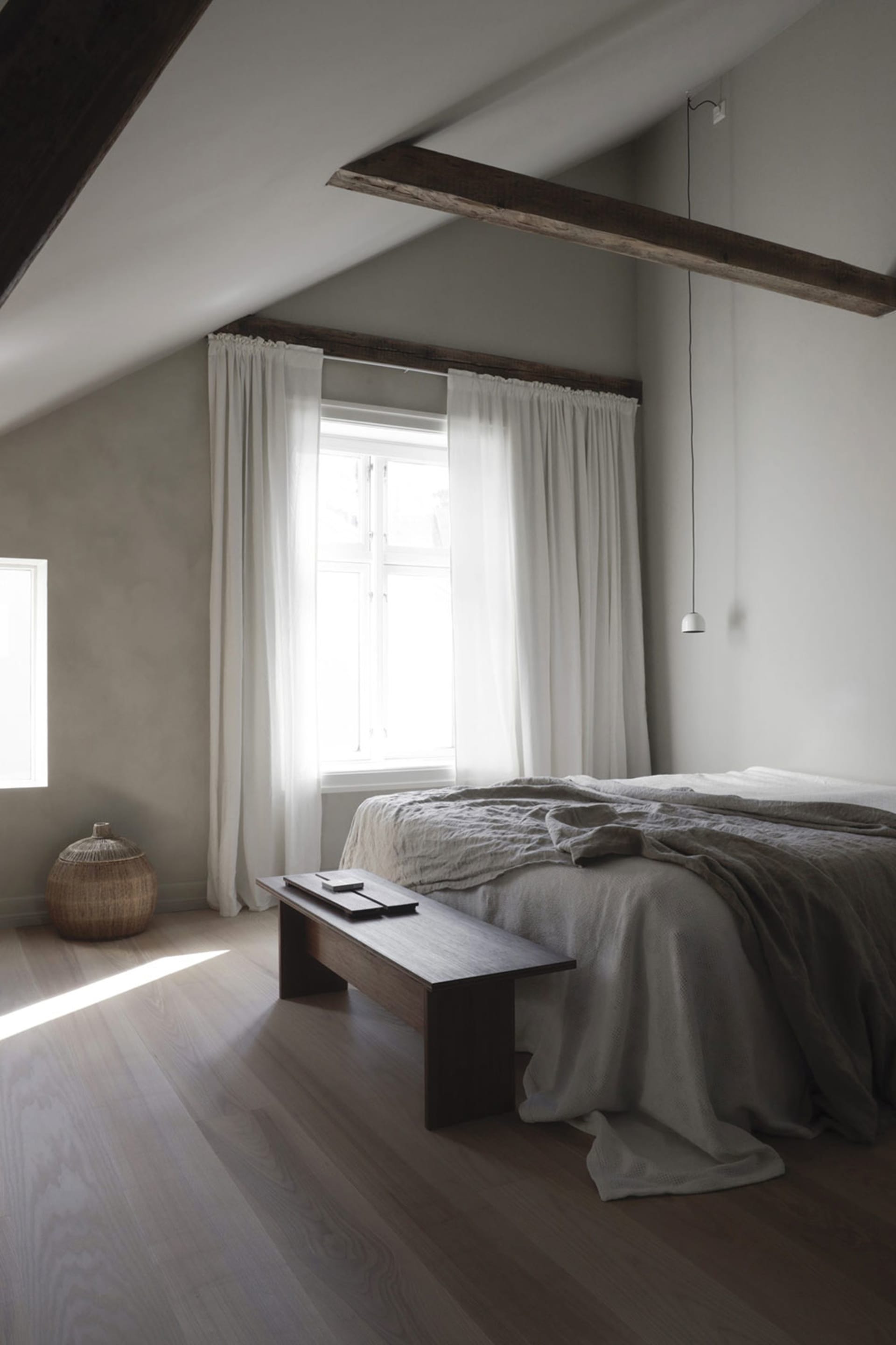 A minimalist bedroom with grey bedding, wooden flooring, and exposed beams.