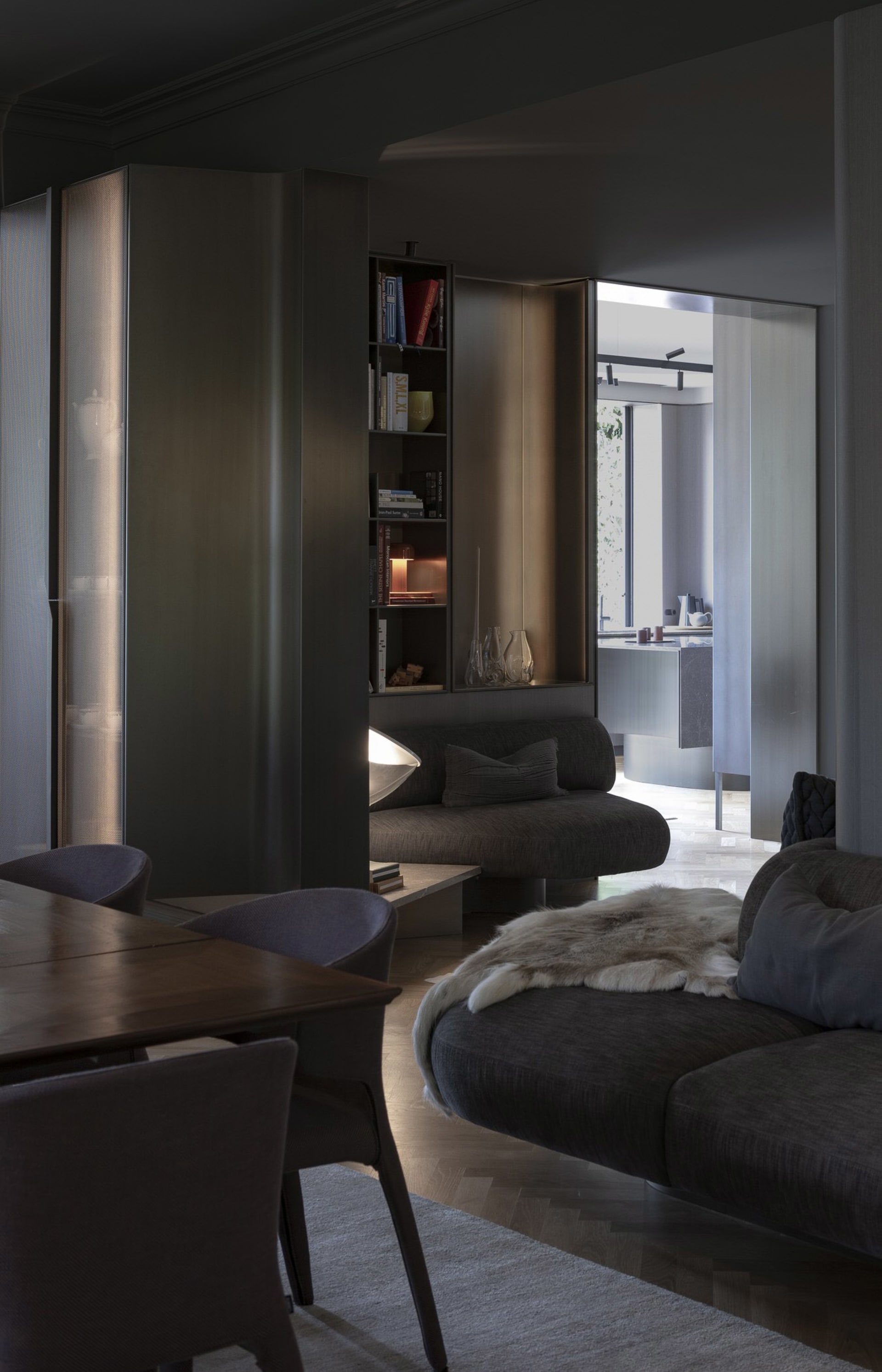 A modern minimalist living room with dark furniture, a bookshelf, and a round sofa with a fur throw.