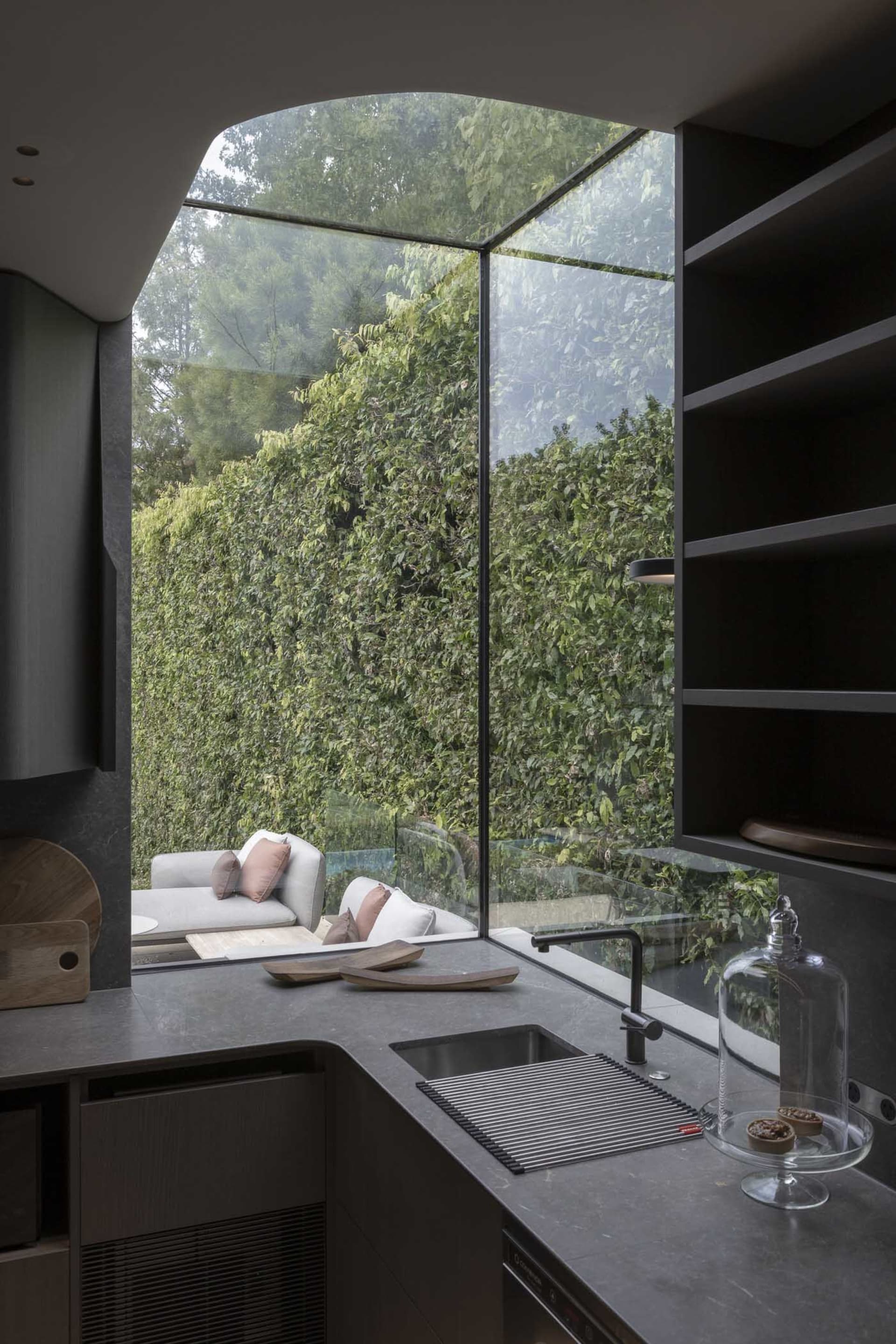 Modern kitchen featuring a large glass window overlooking lush greenery, with a sleek countertop and contemporary cabinetry.