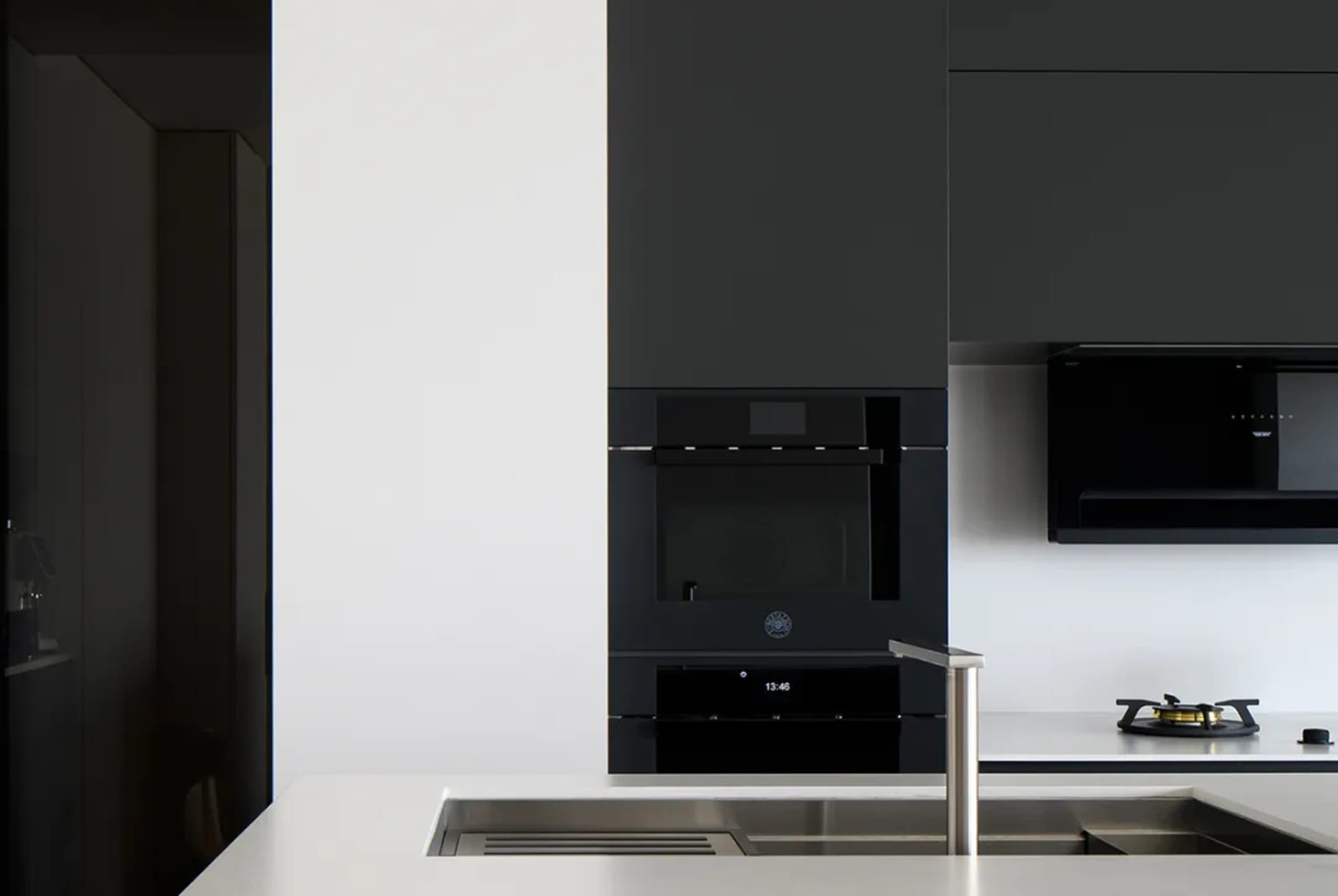 Modern minimalist kitchen with sleek black appliances and white countertops.