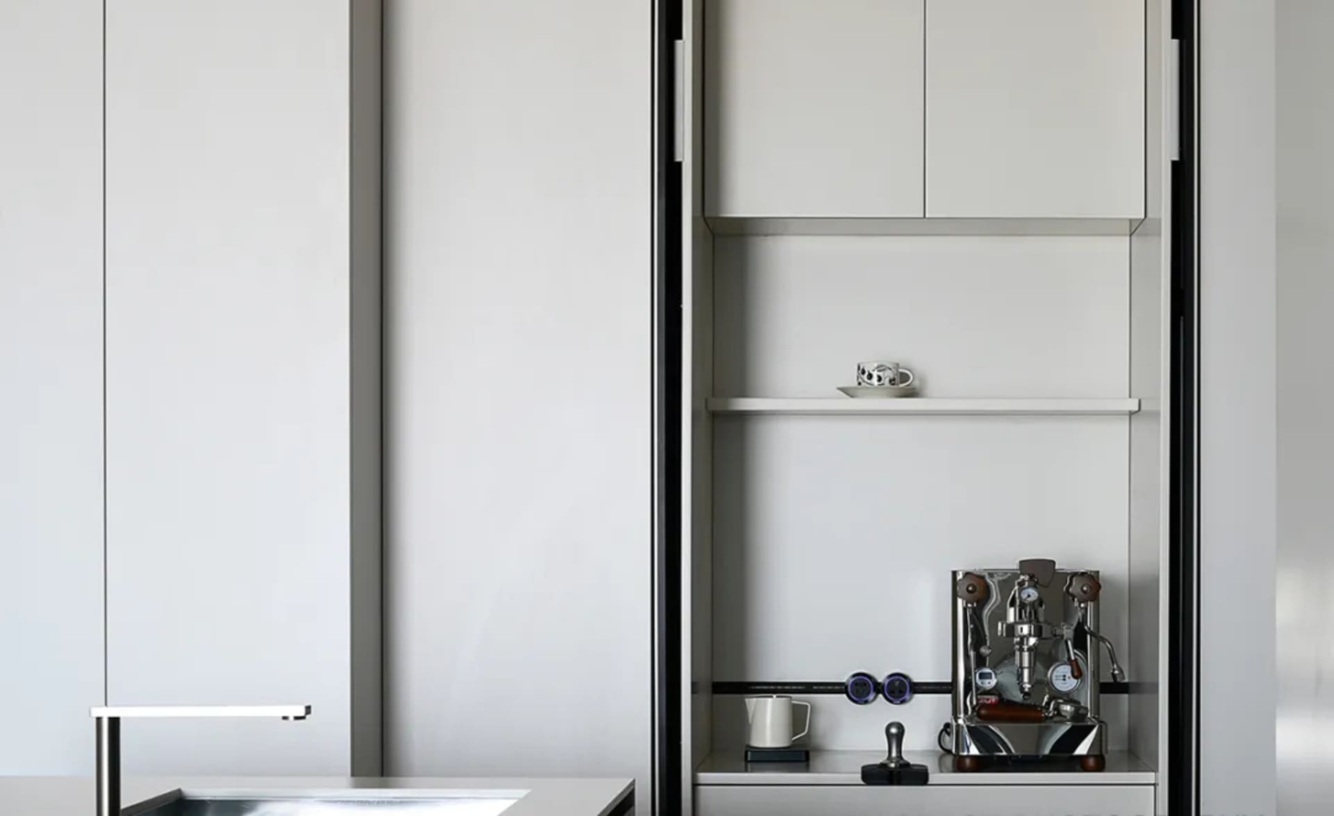 A minimalist modern white kitchen with sleek cabinets and an espresso machine on the countertop.