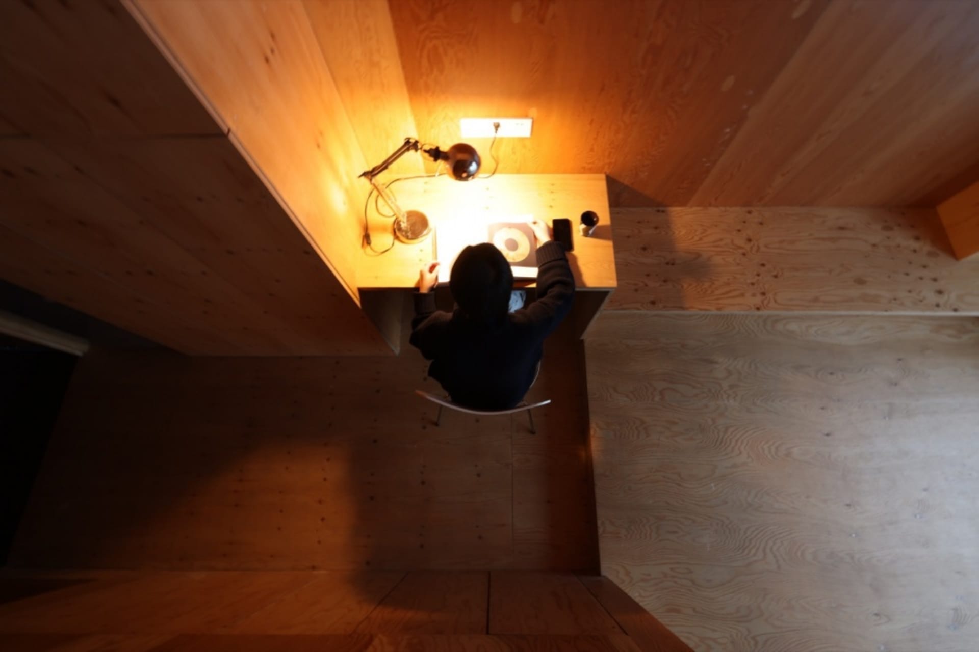 The minimalist workspace is designed with wooden walls and flooring, featuring a compact desk and a simple, white chair.