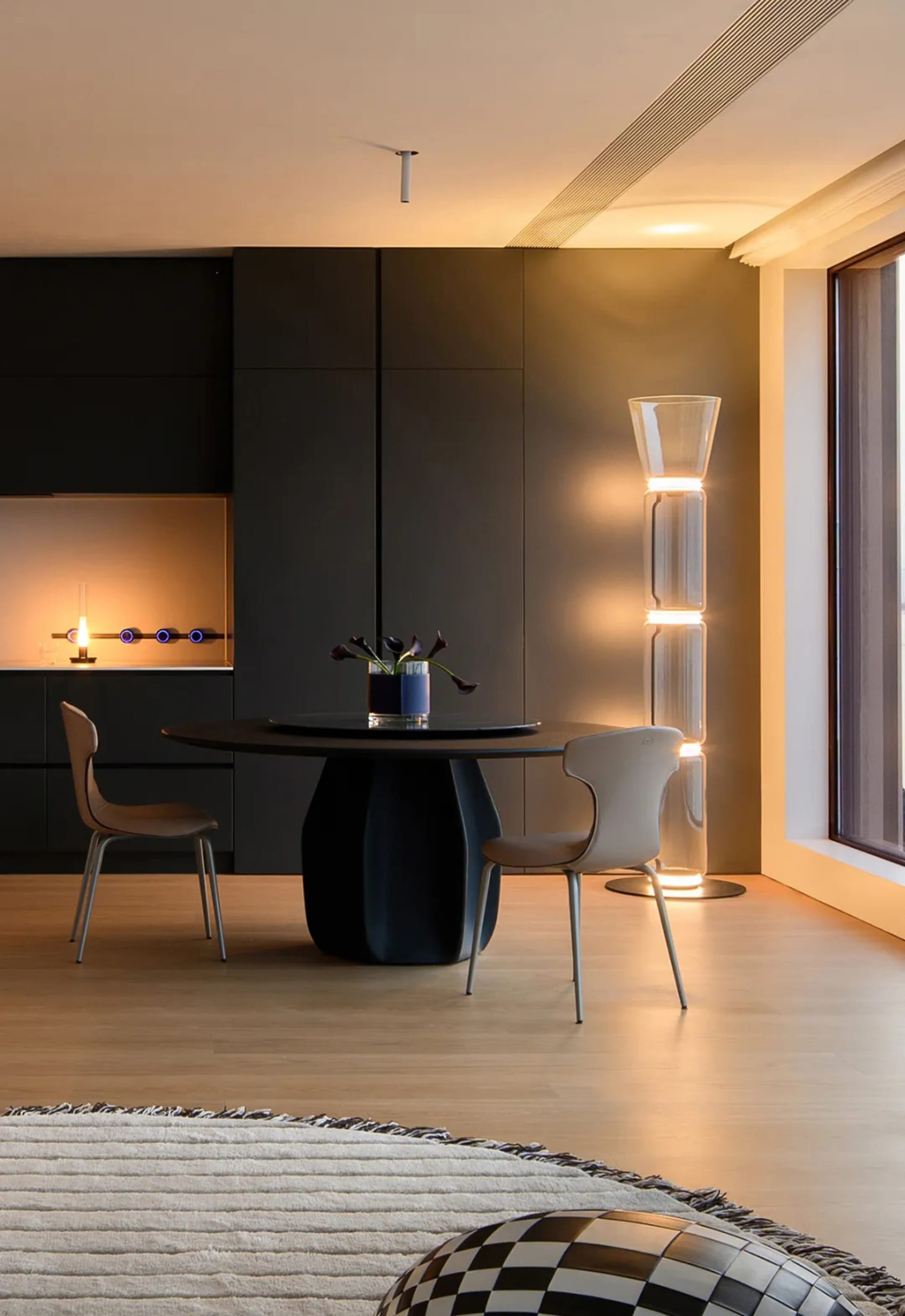 Modern dining room featuring a sleek black table, minimalist chairs, and contemporary floor lamp with illuminated glass tubes