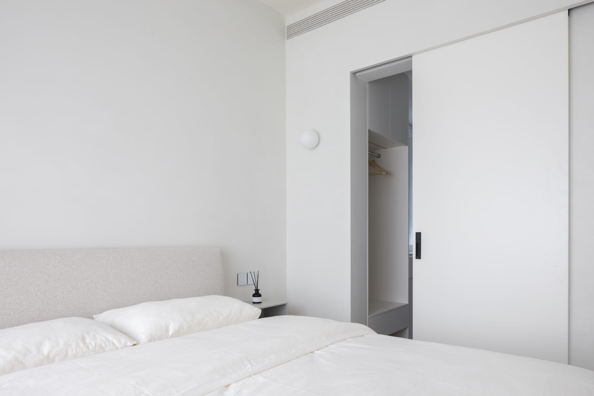 A minimalist bedroom with a bed, white bedding, and a closed closet.