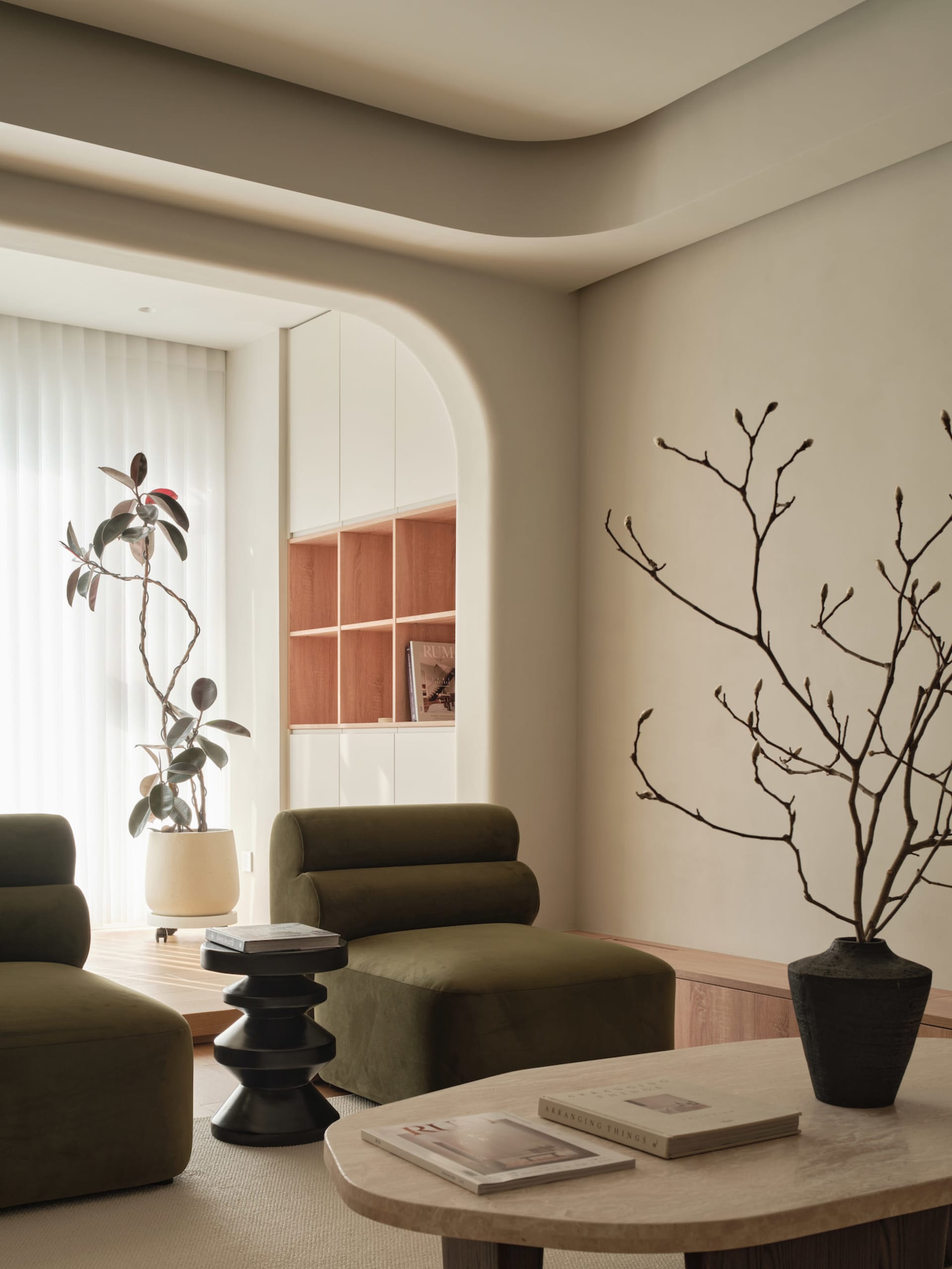 A modern living room with neutral-toned decor and minimalist furniture, featuring green armchairs, a round coffee table, and
