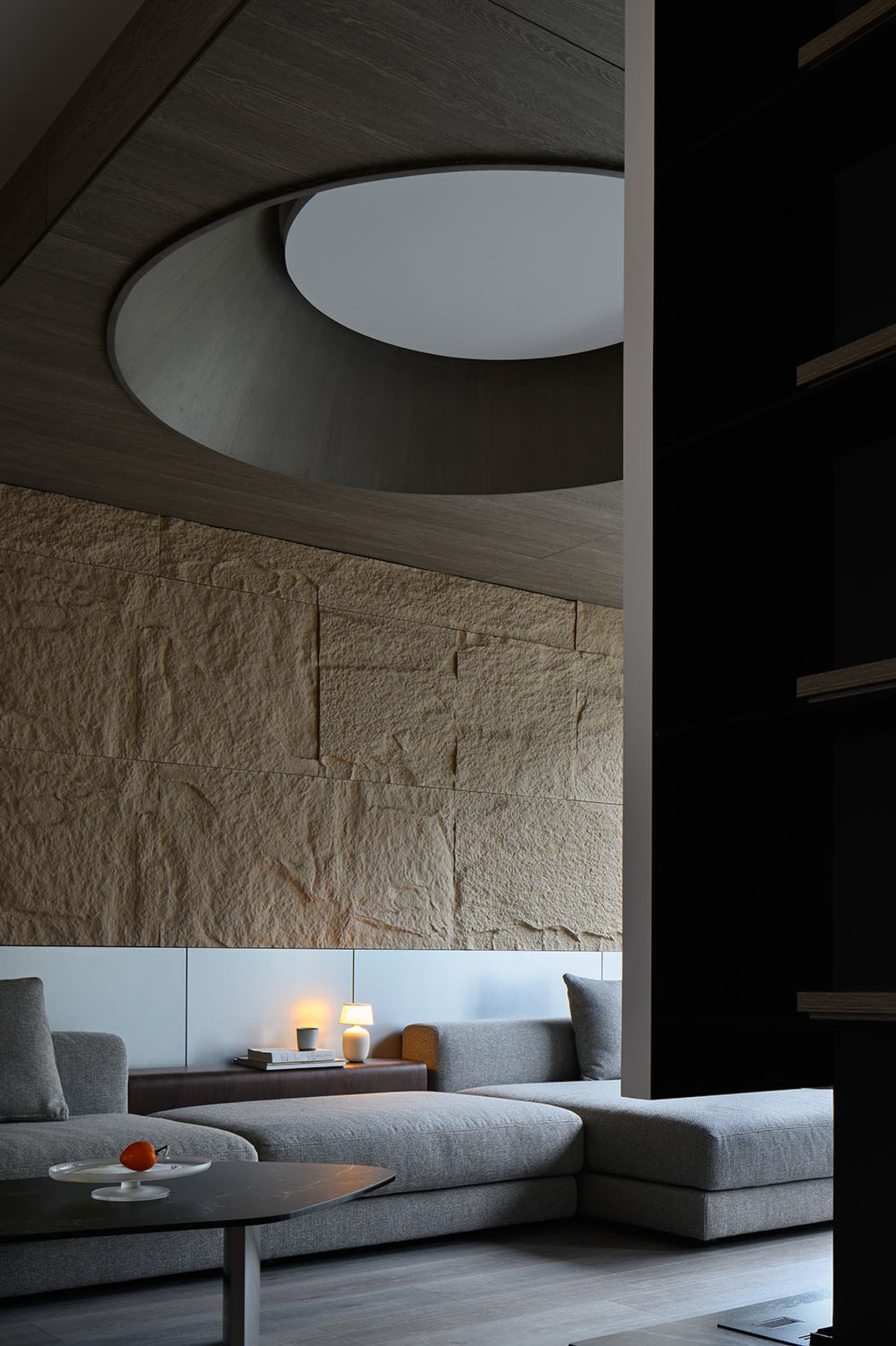 A contemporary living room with stone and concrete materials, featuring a round skylight and a comfortable sectional sofa.
