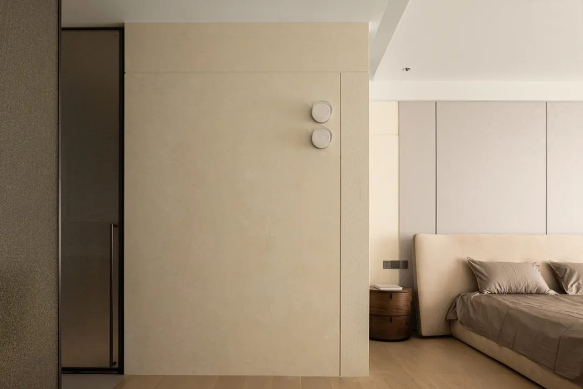 Neutral-toned minimalist bedroom featuring a large bed, side table, and minimalist wall panels.