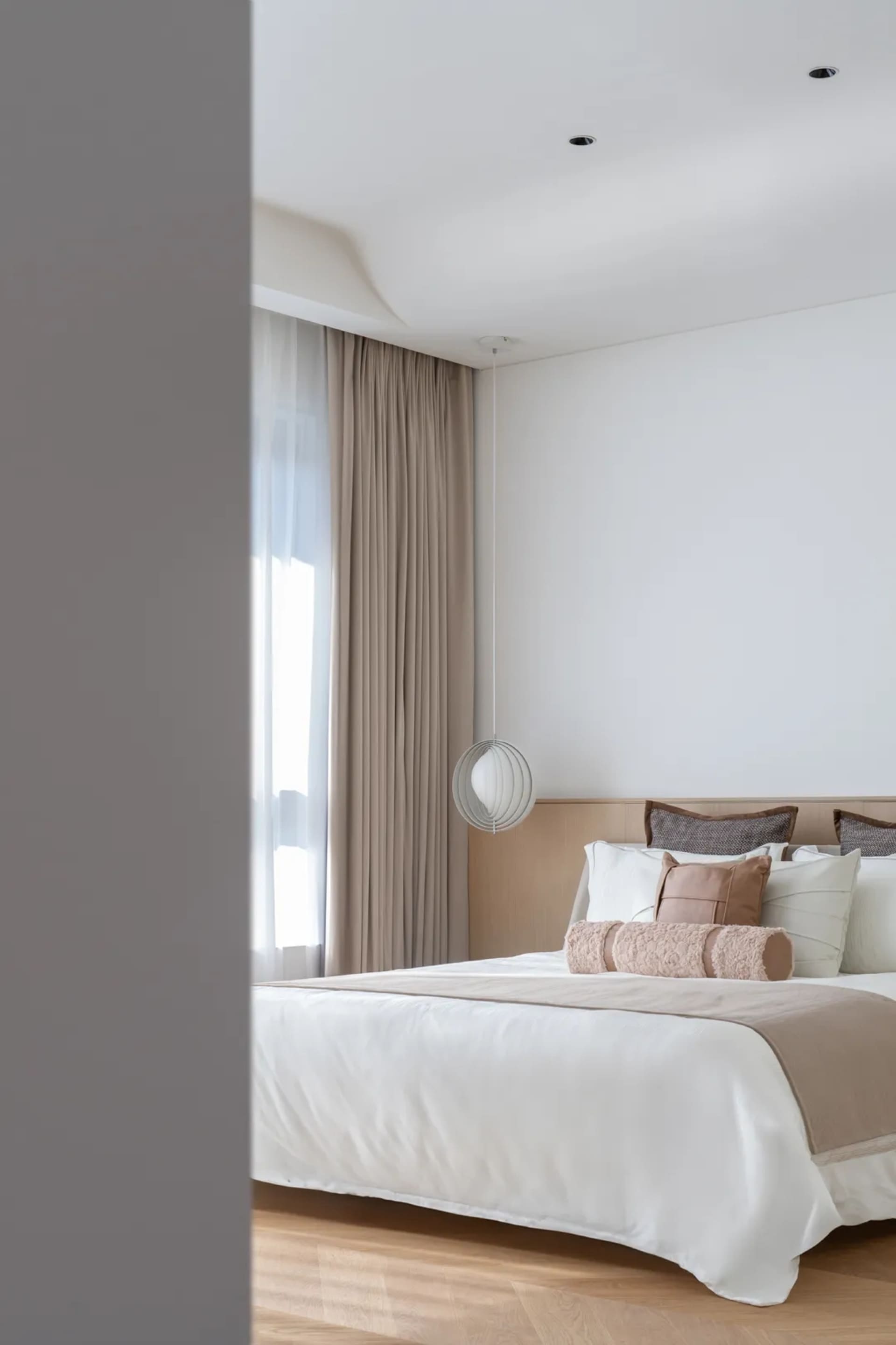 Modern minimalist bedroom with neutral-toned bedding, pillows, and curtains.