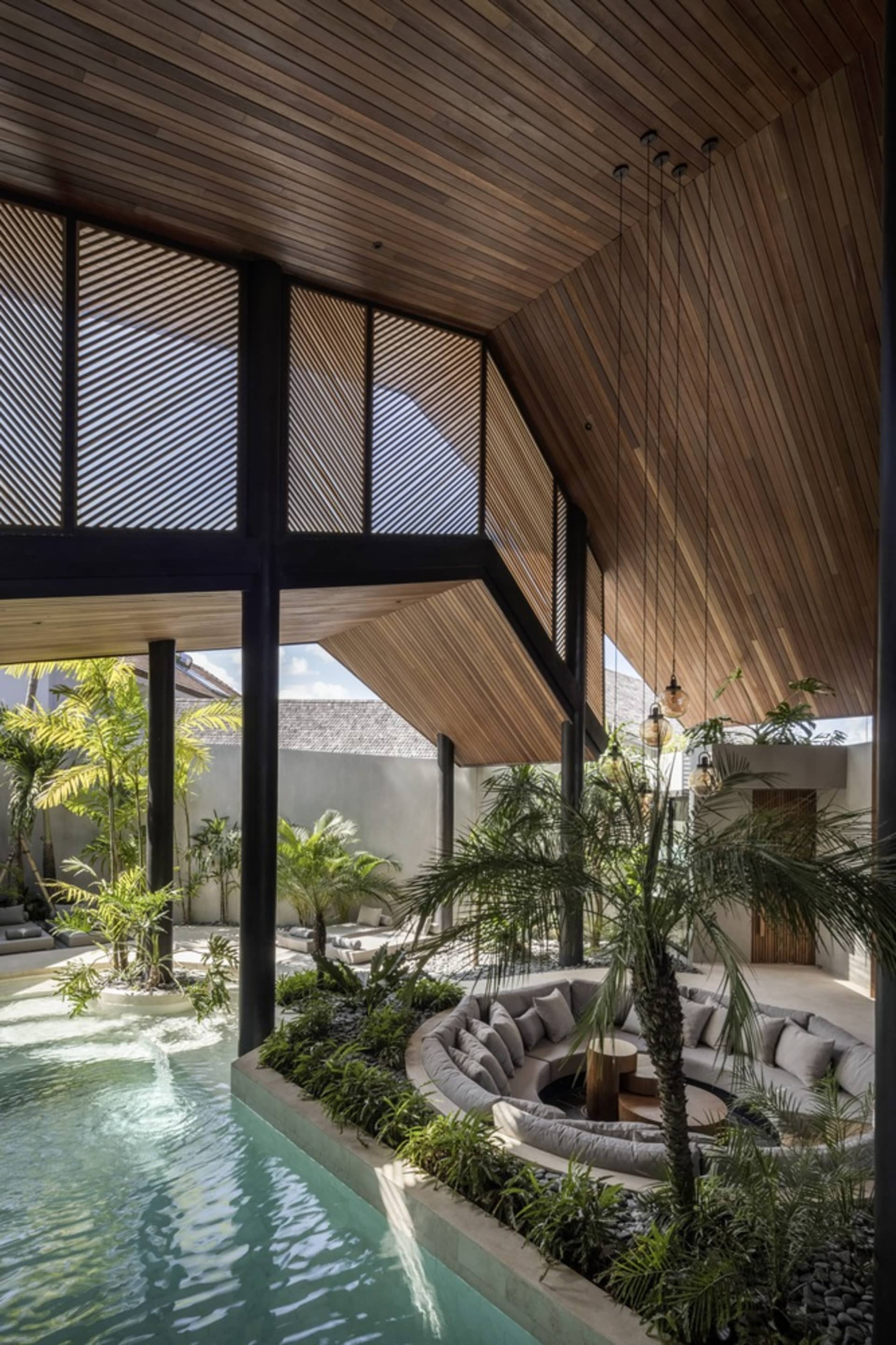 Modern residential interior with a wooden ceiling, curved roof, circular seating area with cushions, and a pool surrounded by