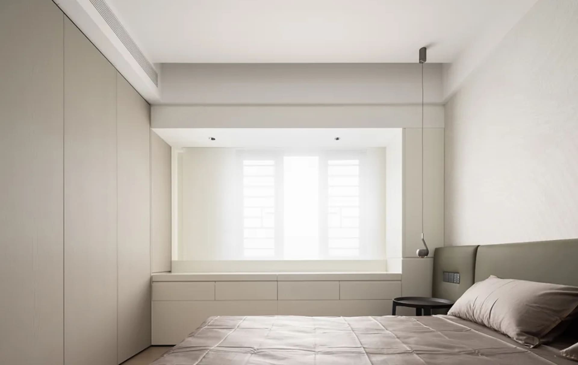 Neutral minimalist bedroom featuring a bed with a simple grey headboard, a window with white shutters, and built-in storage u