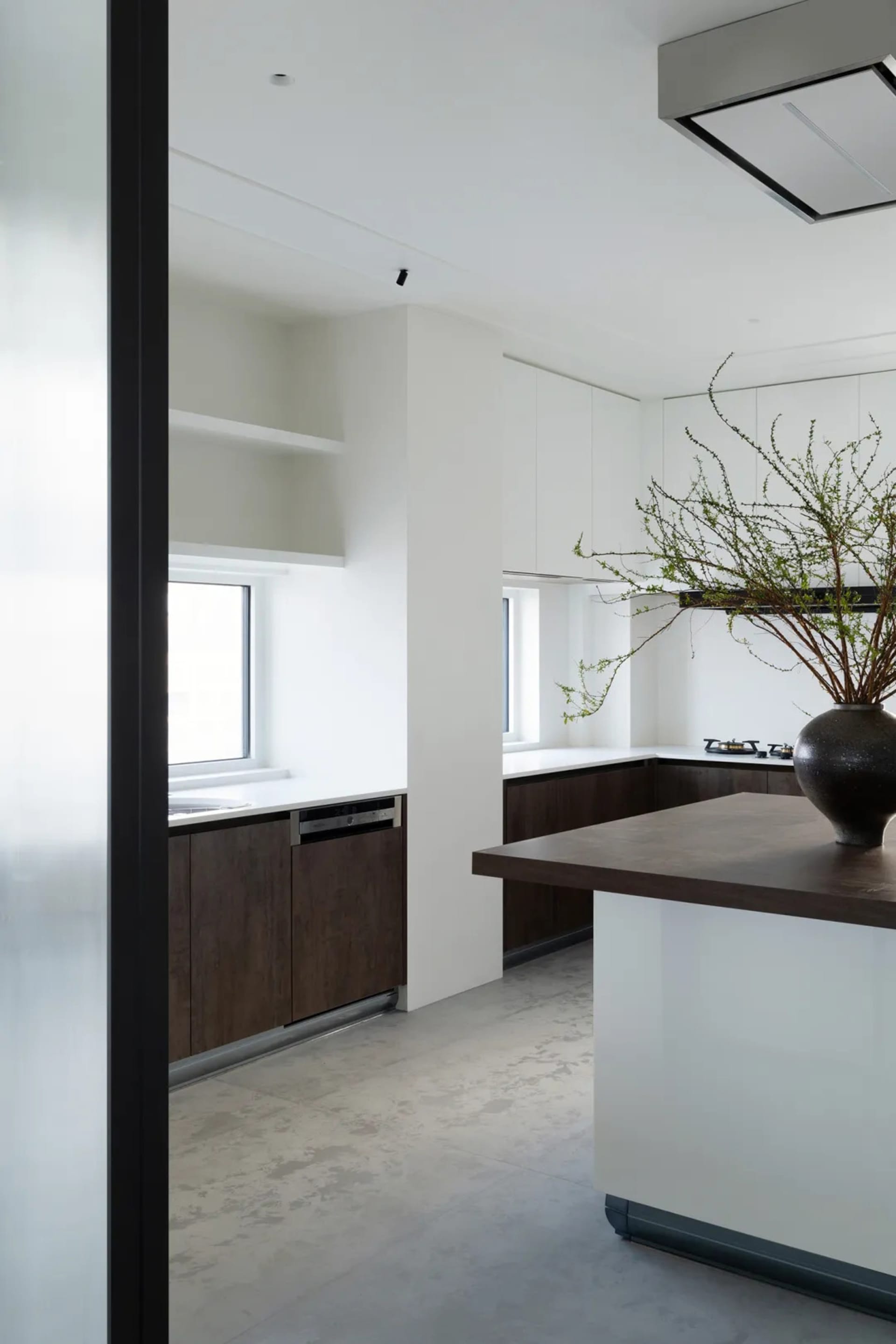 Modern kitchen with minimalist design featuring clean lines, white countertops, dark wood cabinetry, and natural light from t
