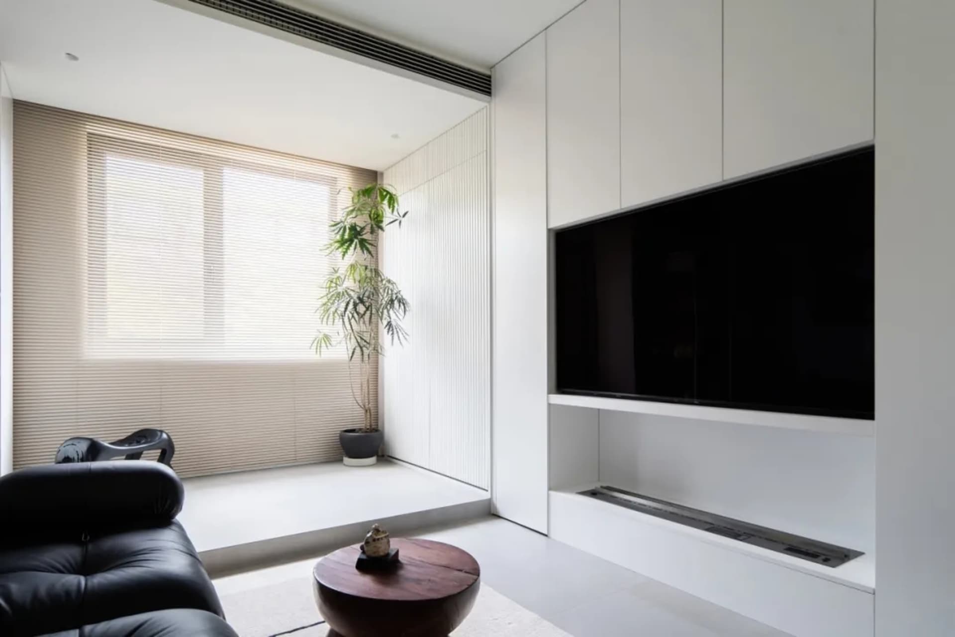A modern living room with a black sofa, wooden coffee table, and white paneled walls.