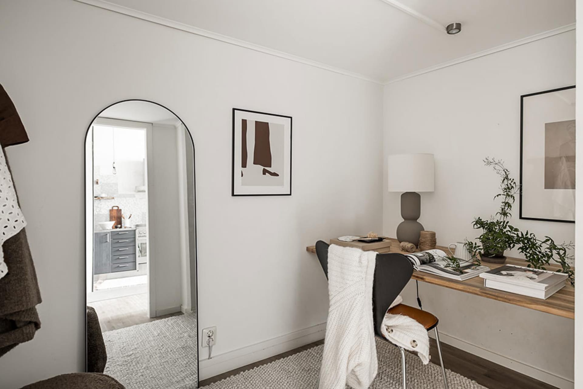 Interior view of a minimalist home office featuring a wooden desk with a leather chair and a white blanket.