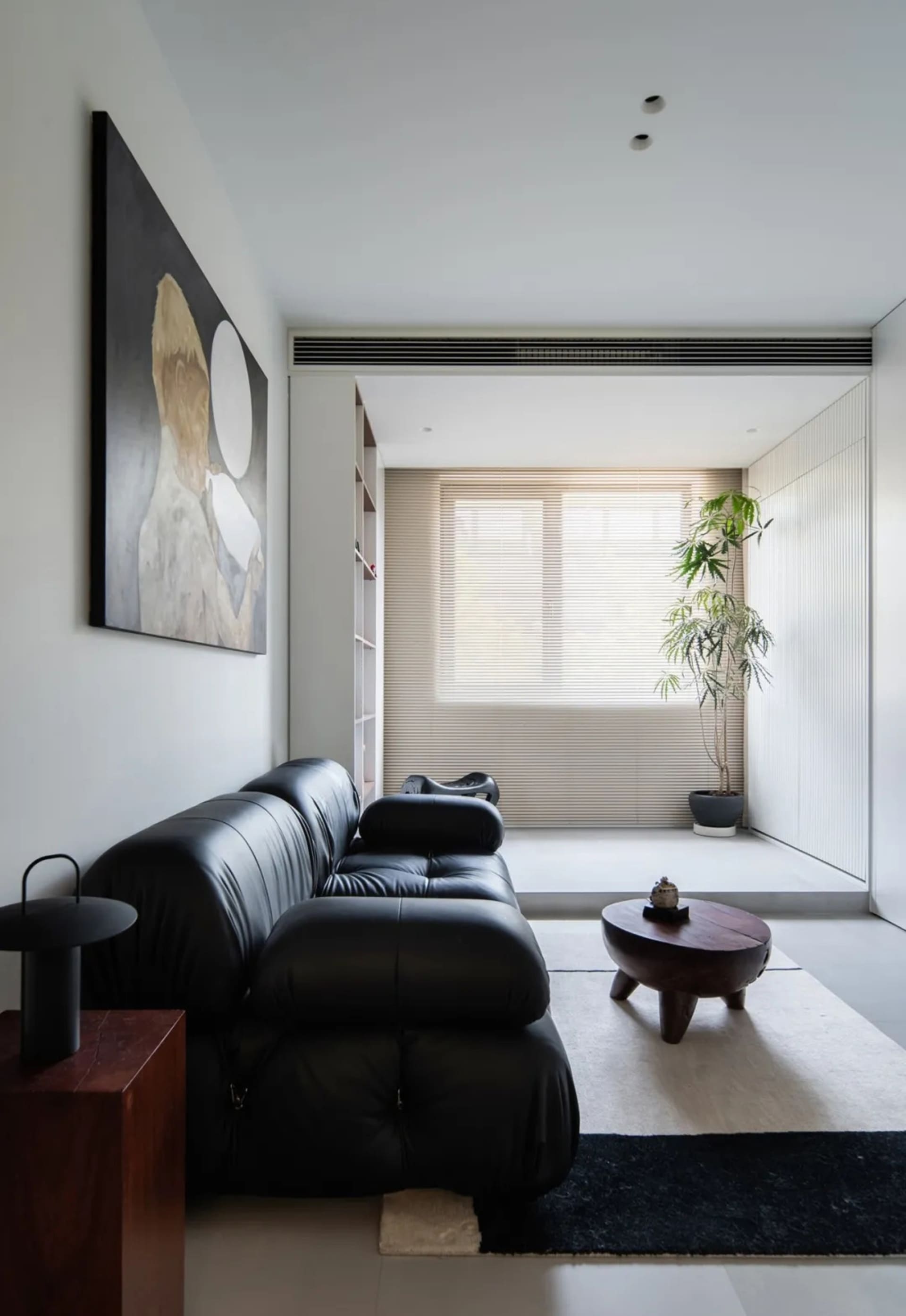 Modern minimalist living room featuring a sleek black leather sofa on a concrete floor, with a round wooden side table and a