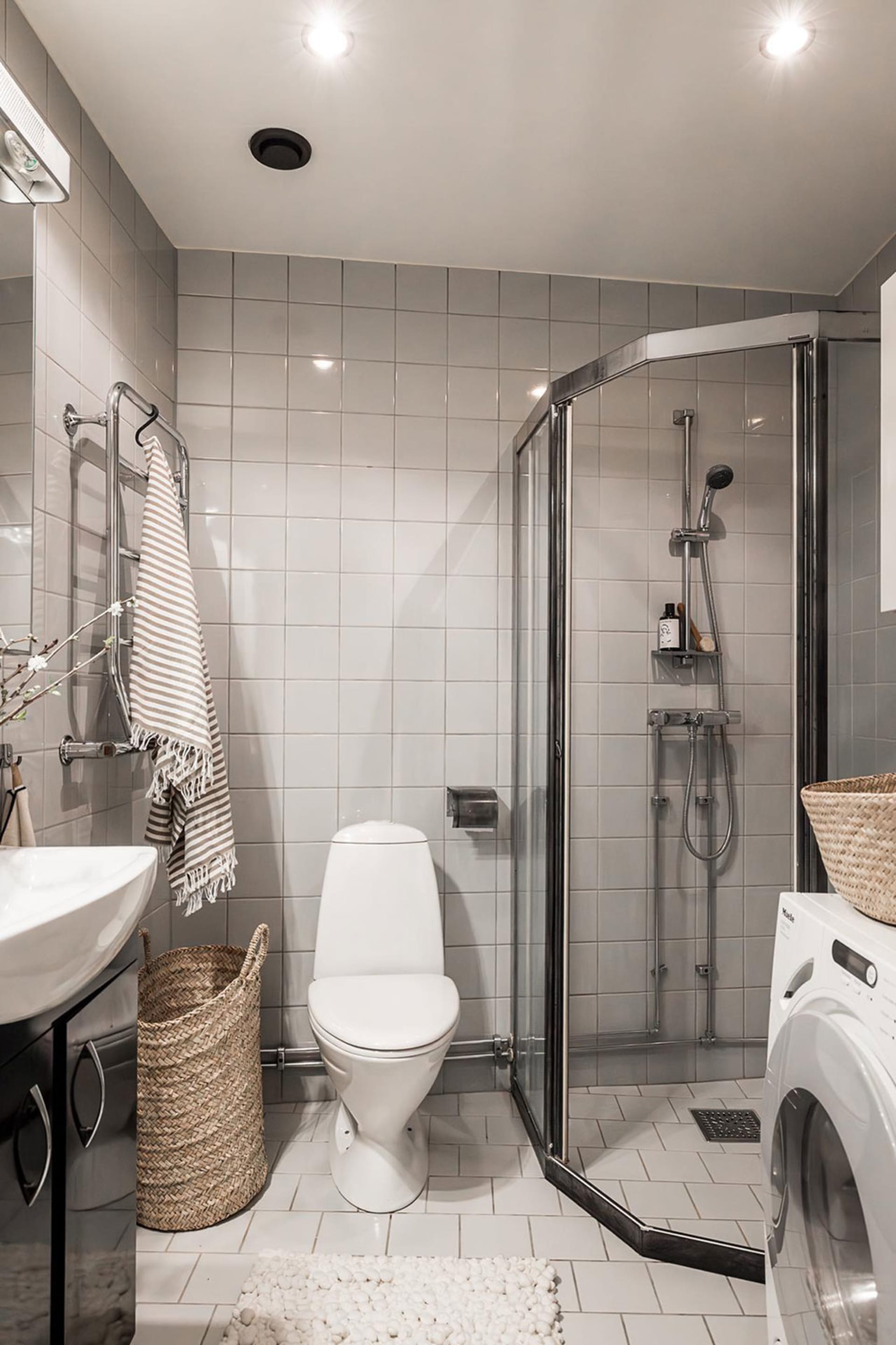 A minimalist bathroom with gray tiles, a white toilet, and a glass shower door.