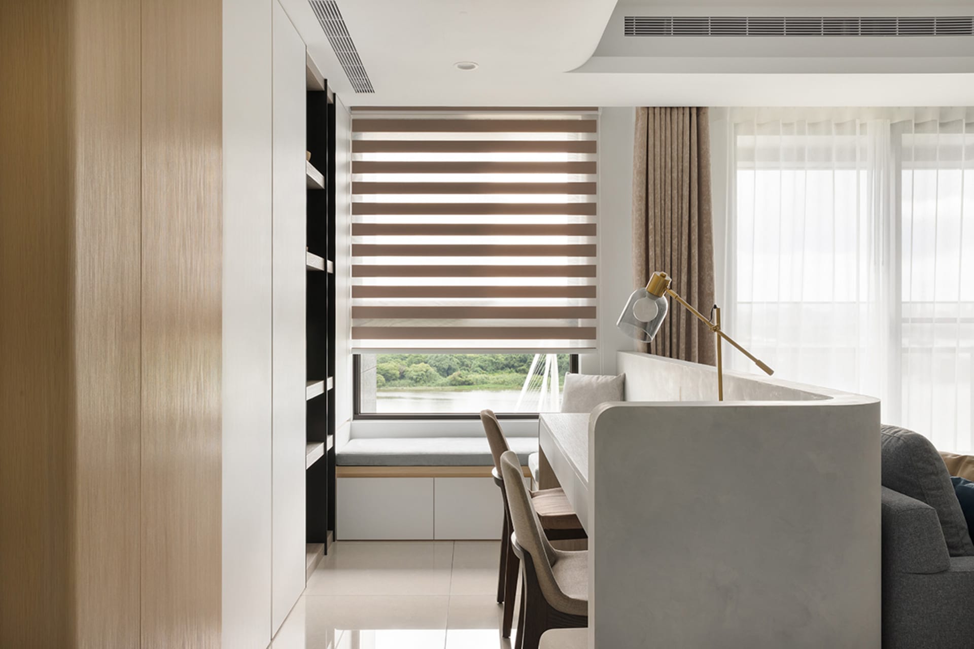 A modern dining room featuring white and light wood elements, with a window overlooking a scenic view and a lamp providing il