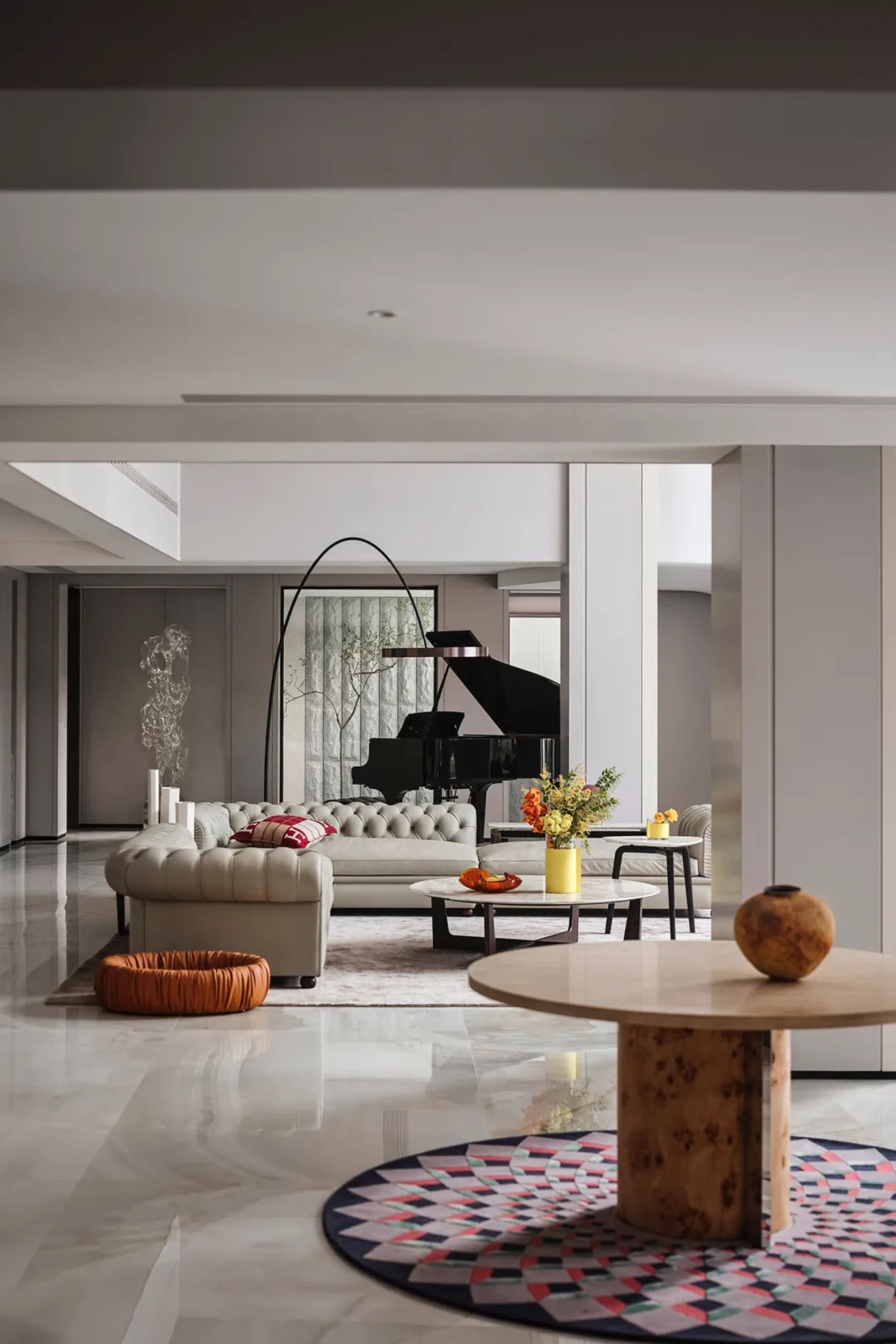 A modern living room featuring marble furniture, including a round table on a colorful patterned rug and a piano in the backg