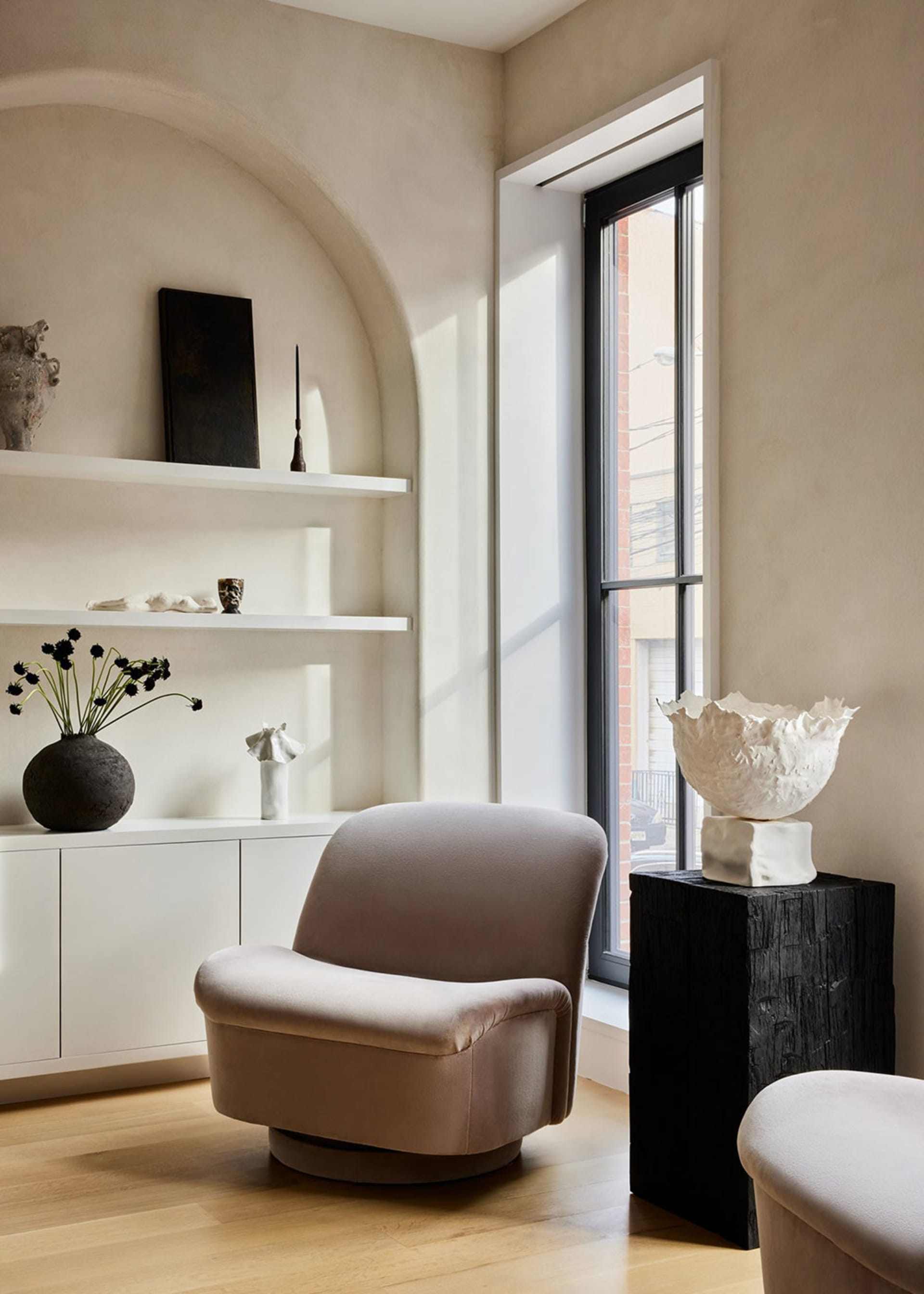 A modern minimalist lounge room with a beige chair, white shelves, and decorative items.