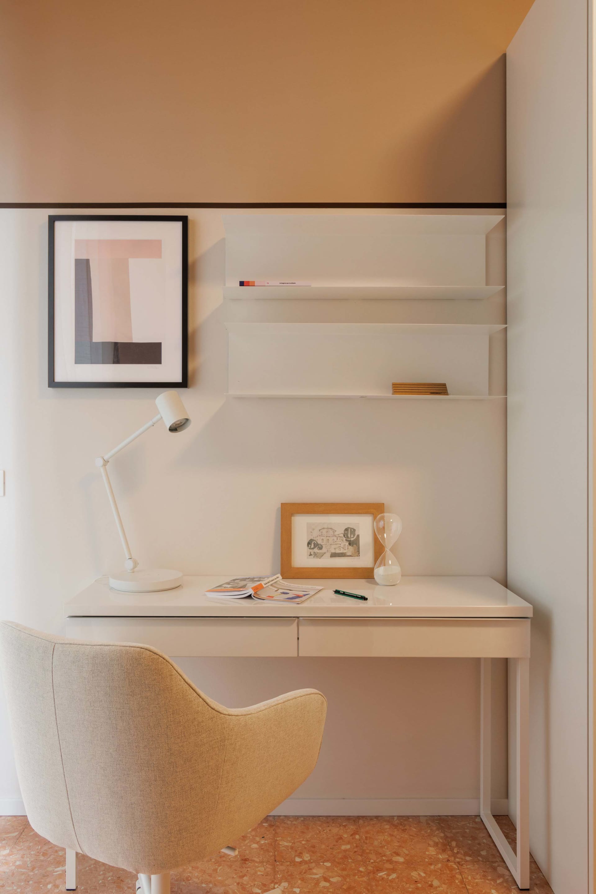 A modern home office setup with a white desk, minimalist shelves, and a beige chair.