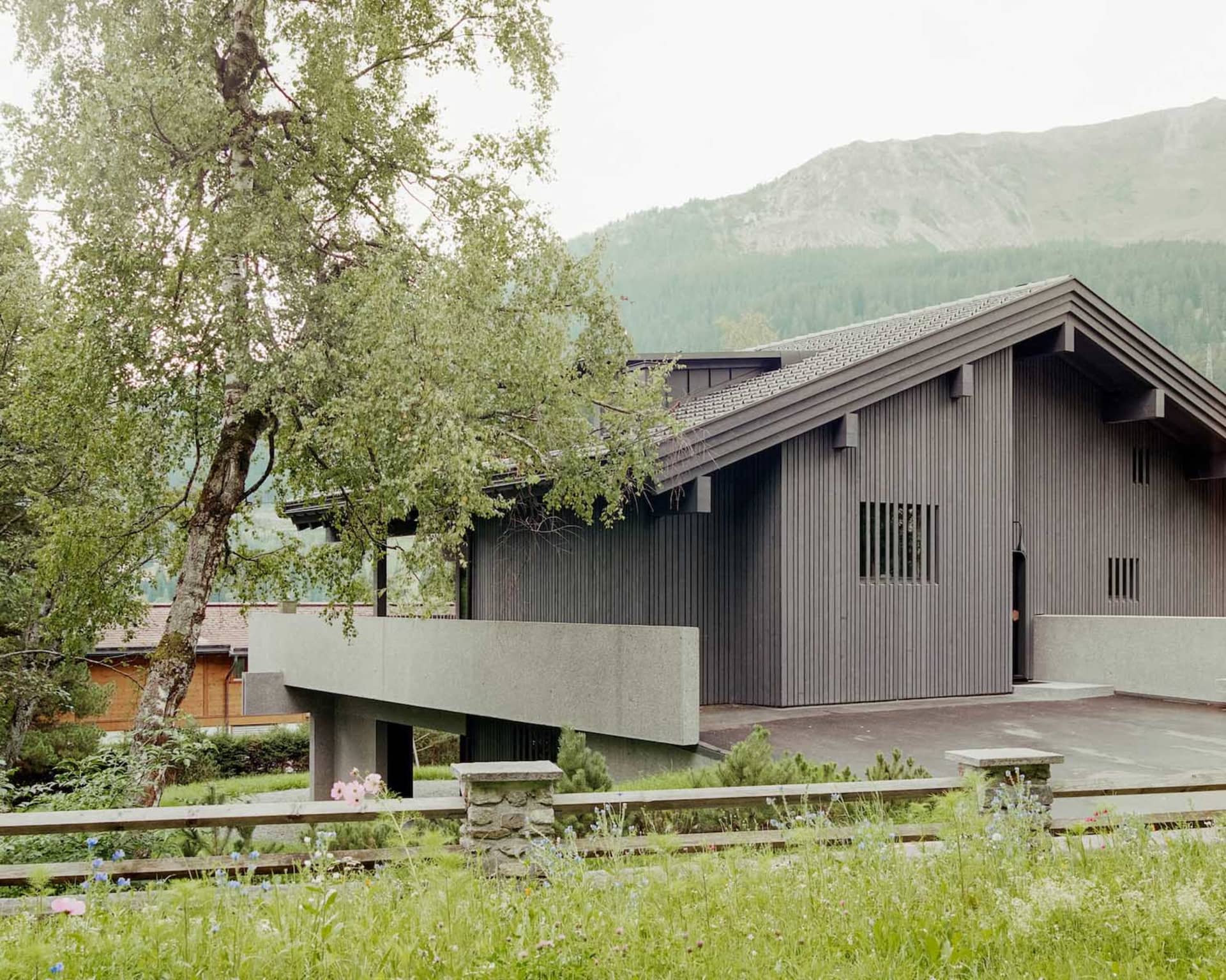 A modern house with metal siding and a concrete patio in a mountainous landscape.