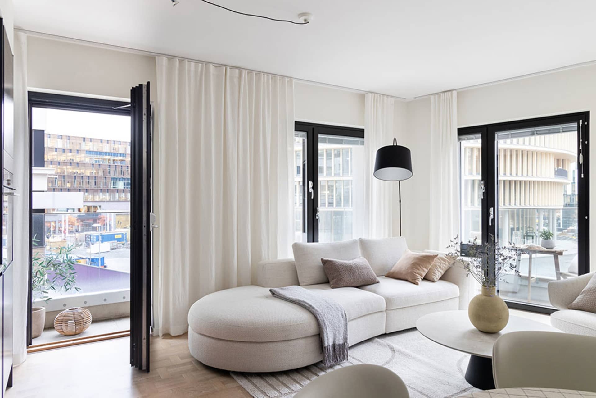 A modern living room with white furniture, fabric upholstery, and large windows.