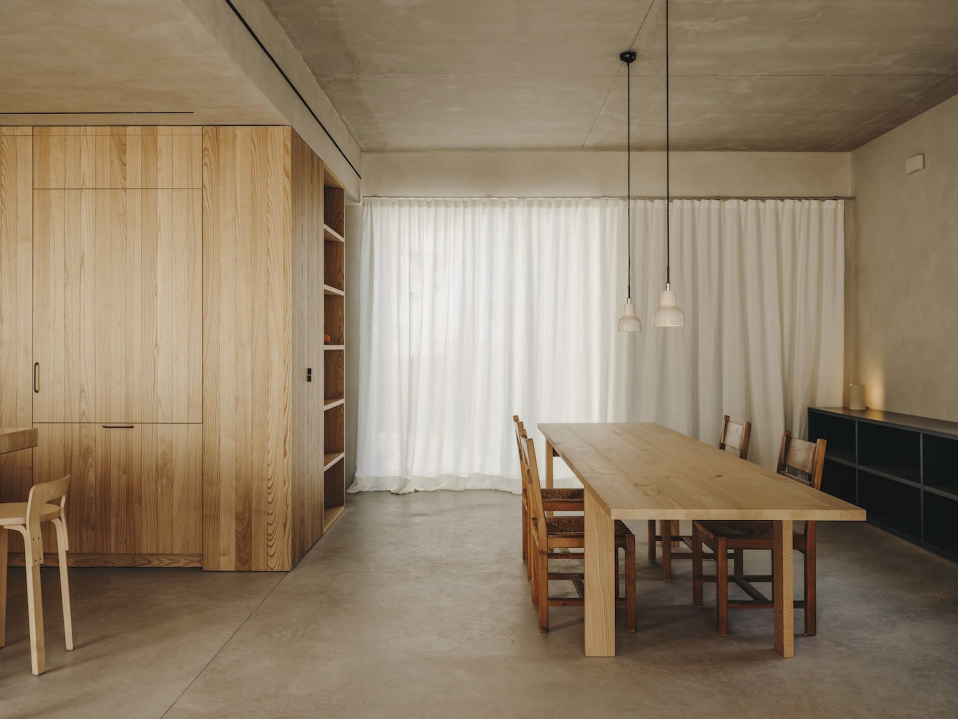 Interior view of a minimalist dining room with wooden furniture and white curtains.