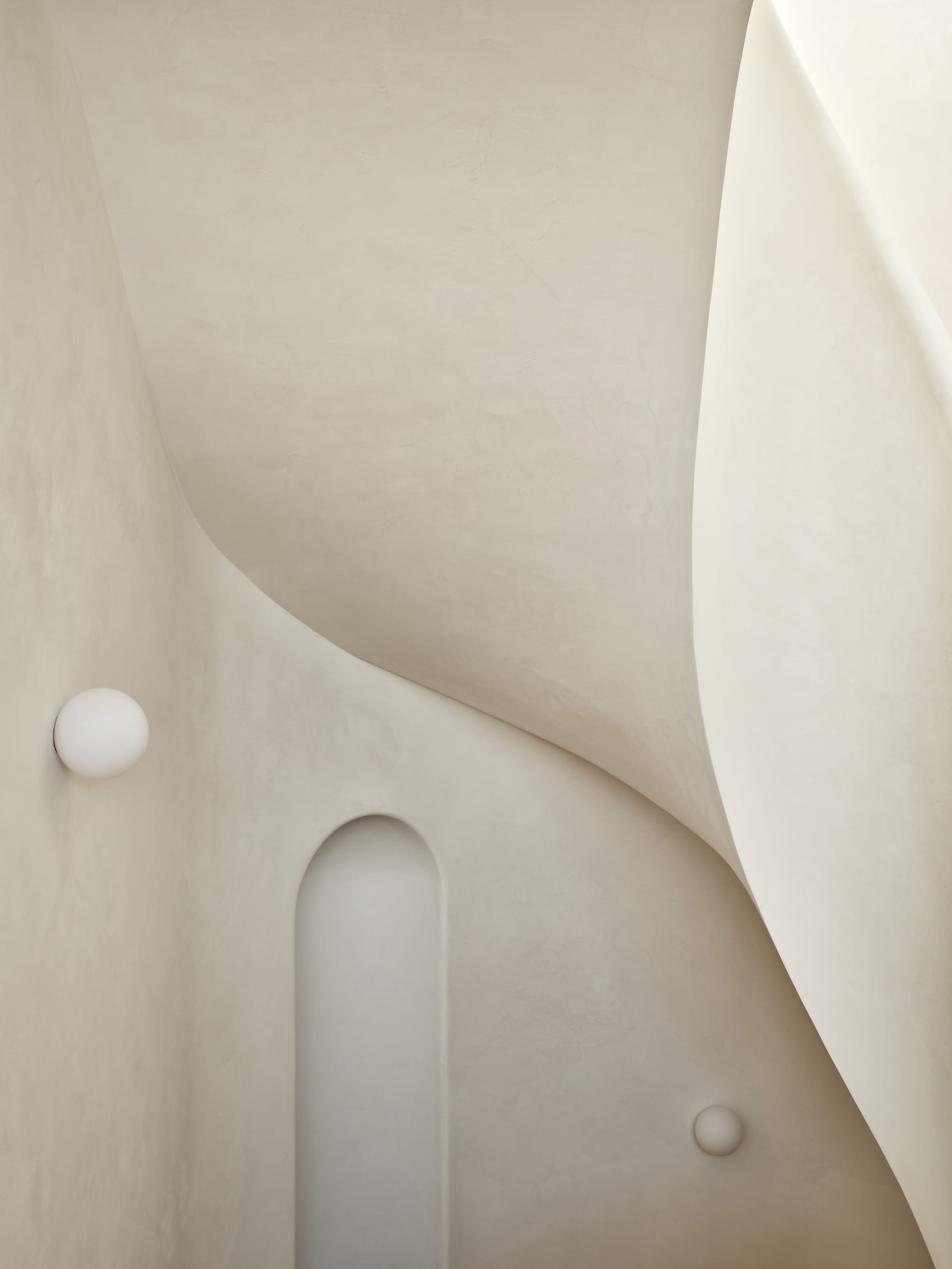 A minimalist bedroom with textured concrete walls and a soft, warm lighting fixture.