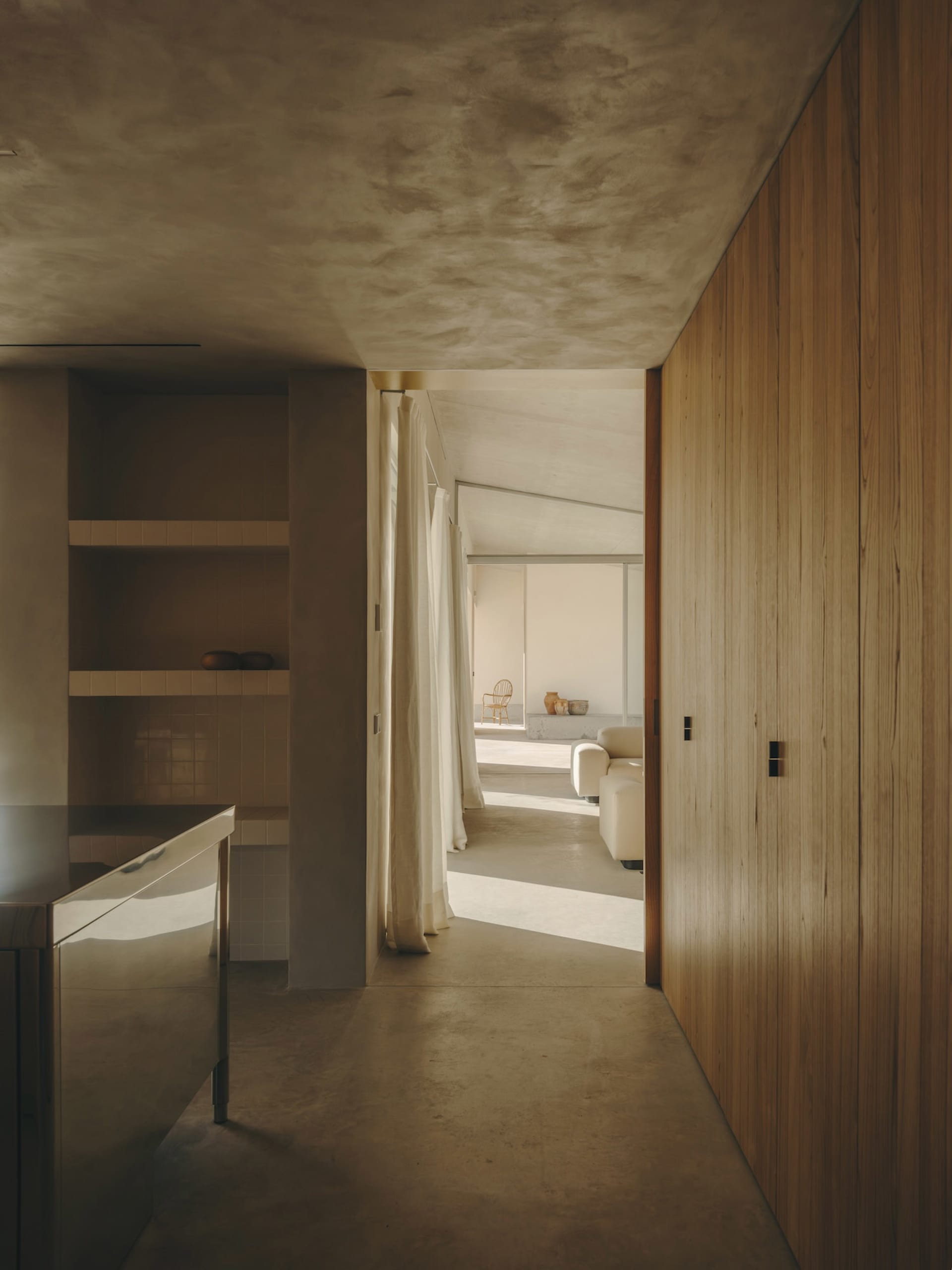 A minimalist living room with concrete walls, wooden paneling, and large windows.