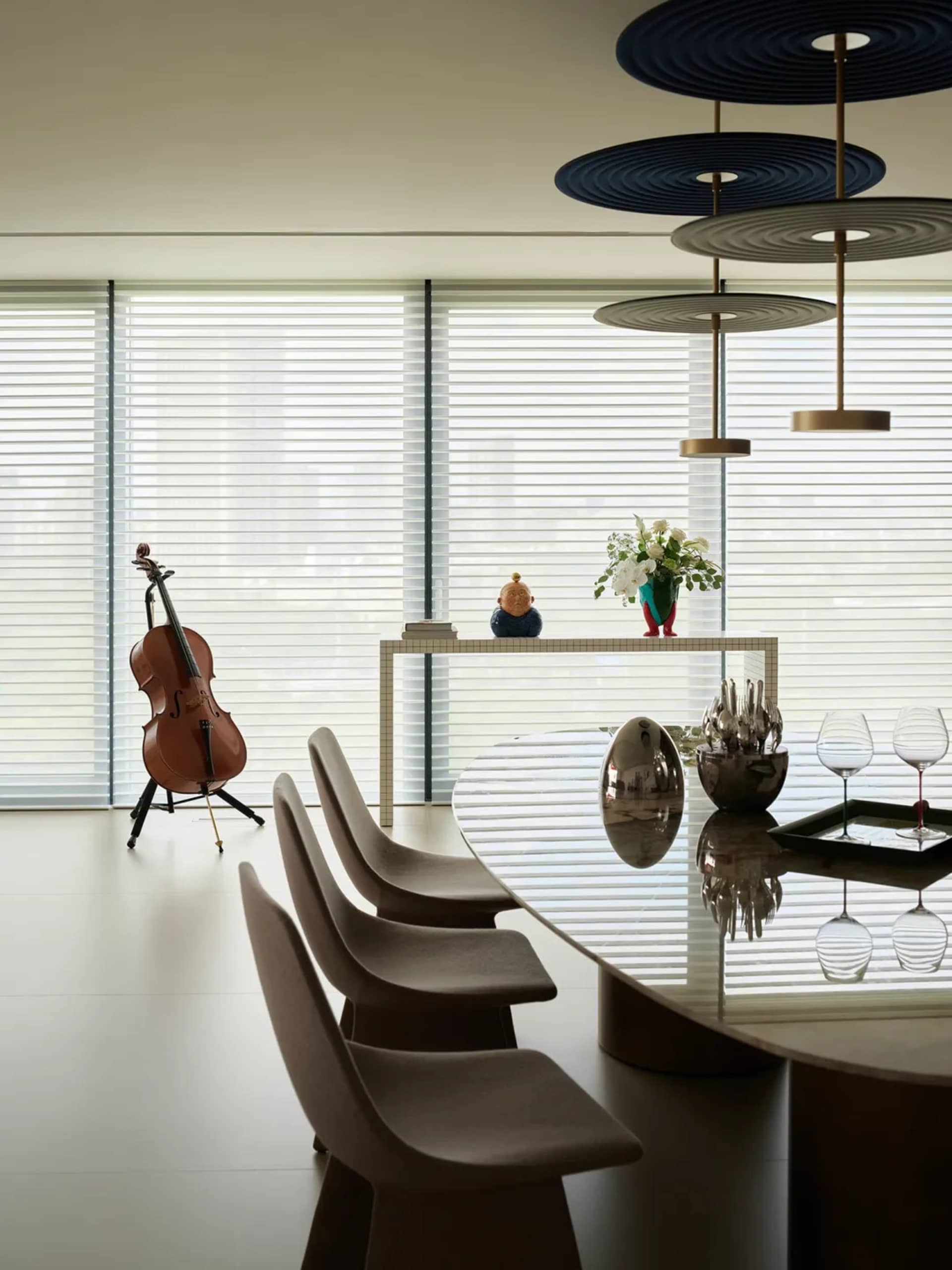 A minimalist dining room featuring a glass table, modern chairs, and decorative elements like a cello, vase, and cutlery.
