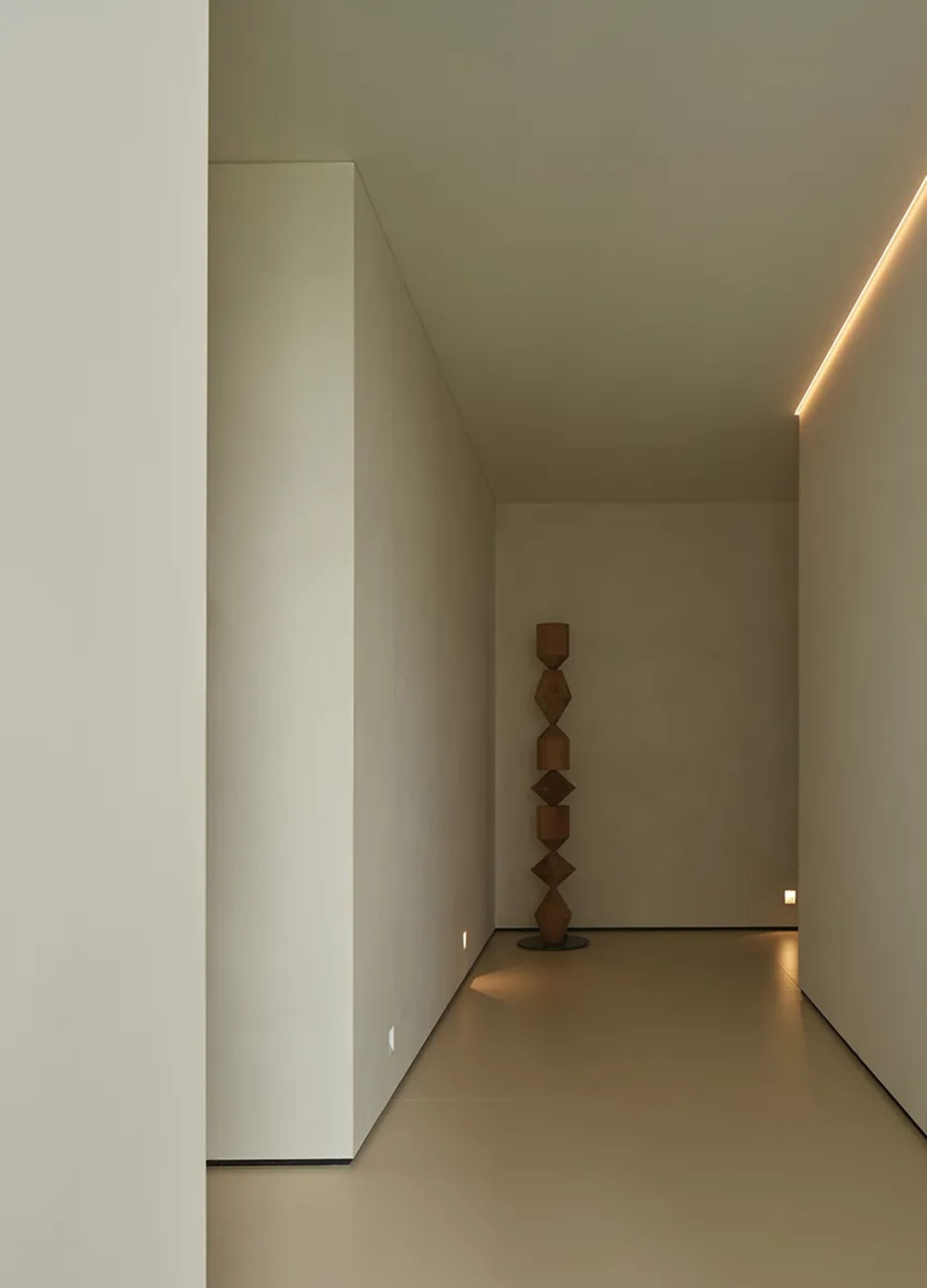 A minimalist hallway features a wooden sculpture and warm lighting.