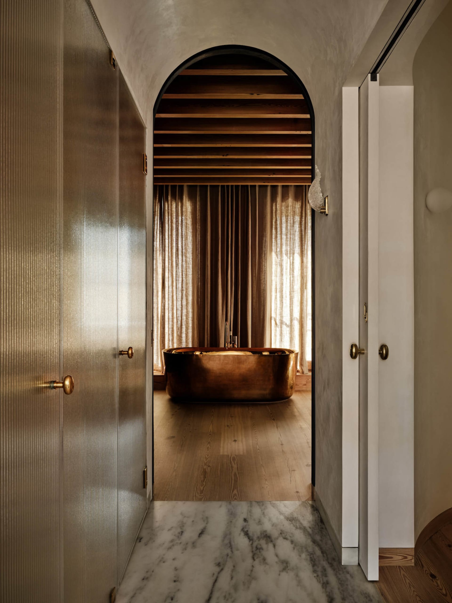 Modern bathroom with a brass bathtub and marble flooring.