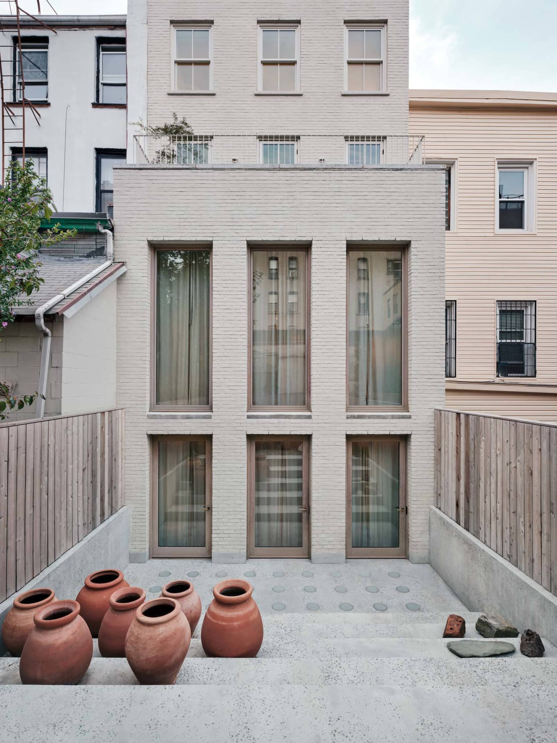 Modern brick townhouse exterior with large windows and terracotta pots in the foreground.