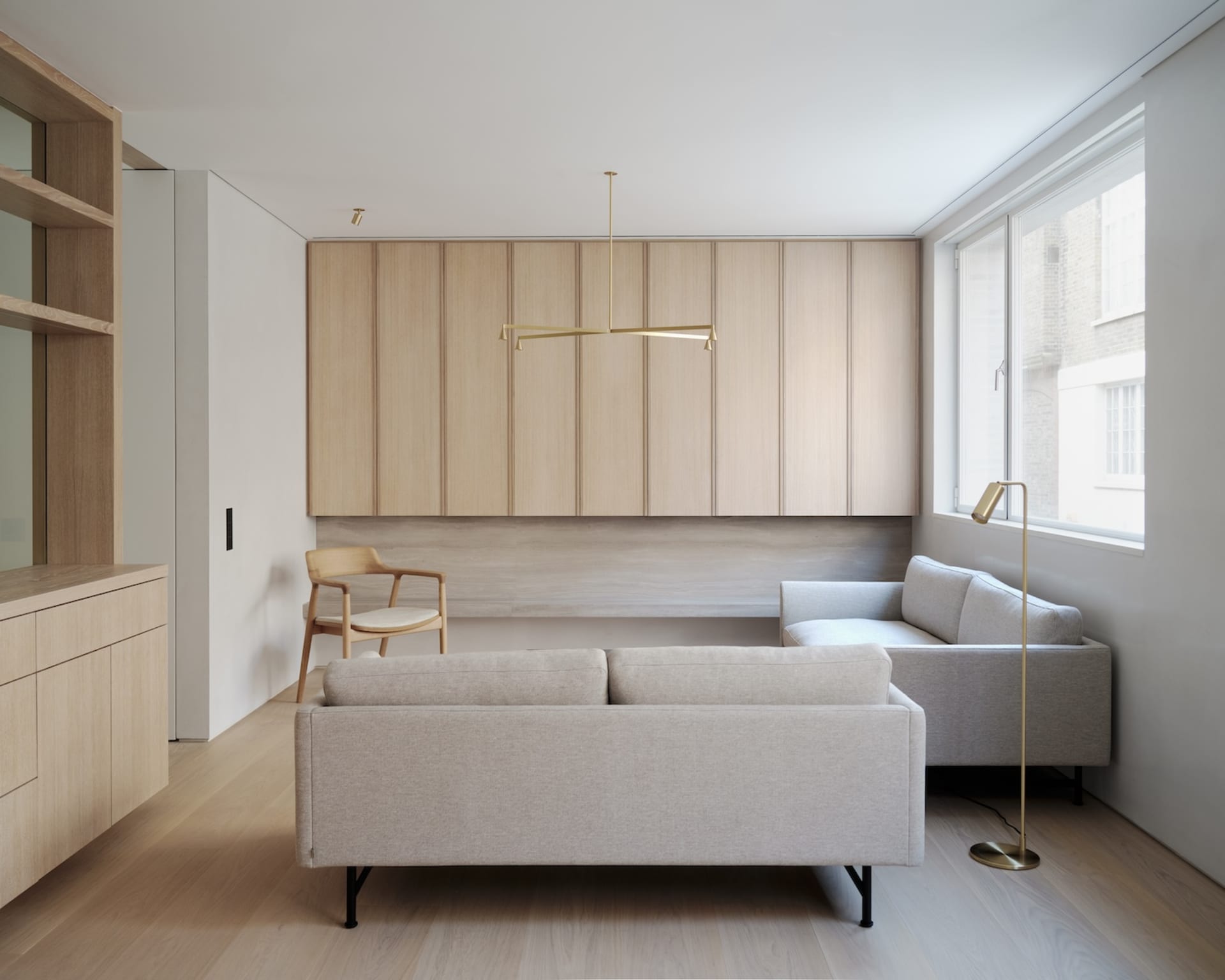Modern minimalist living room with light-colored wooden flooring, light-colored sofas, and a wooden counter with built-in sto