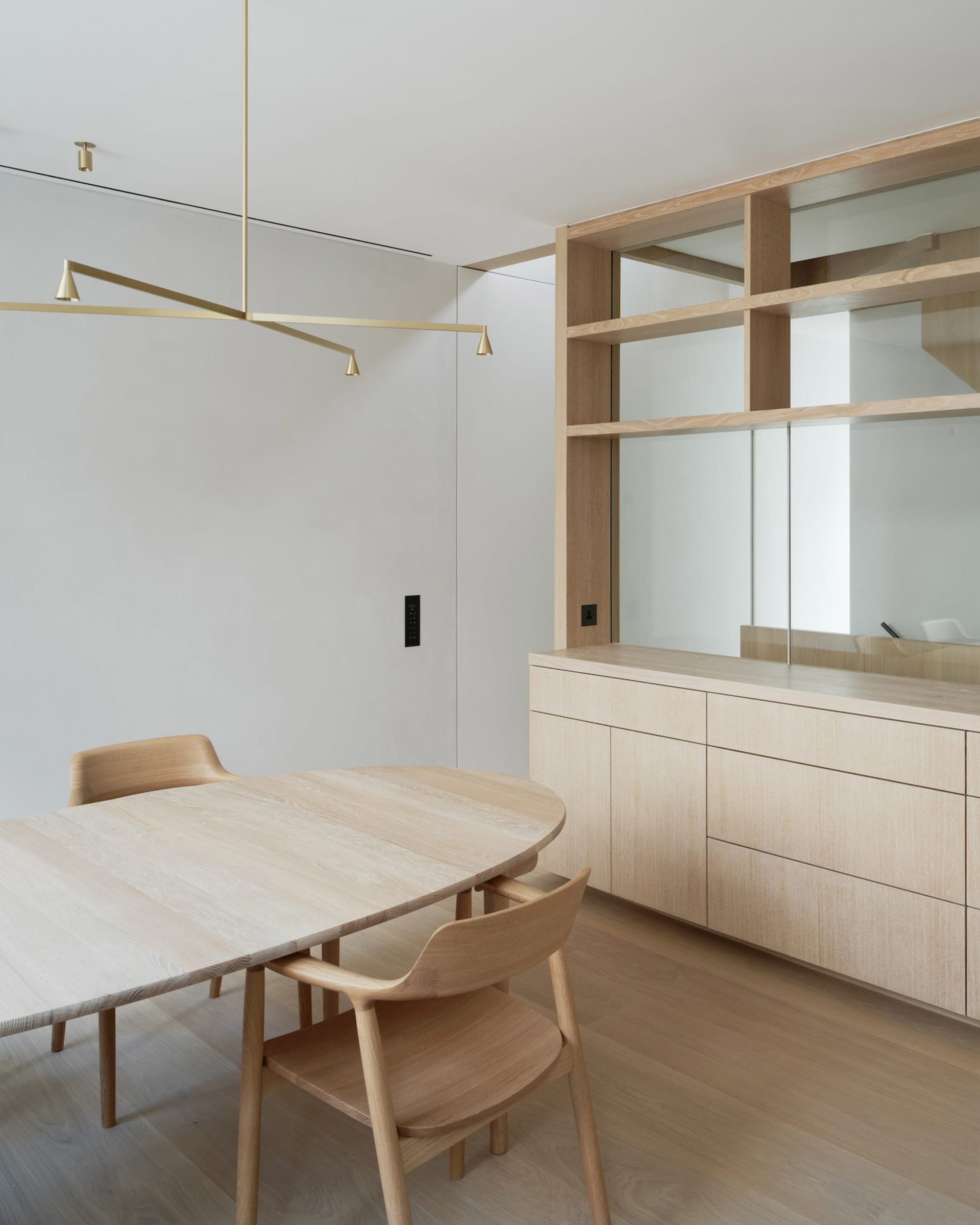 A minimalist living room with a light wood table and chairs, and a wall-mounted lamp.