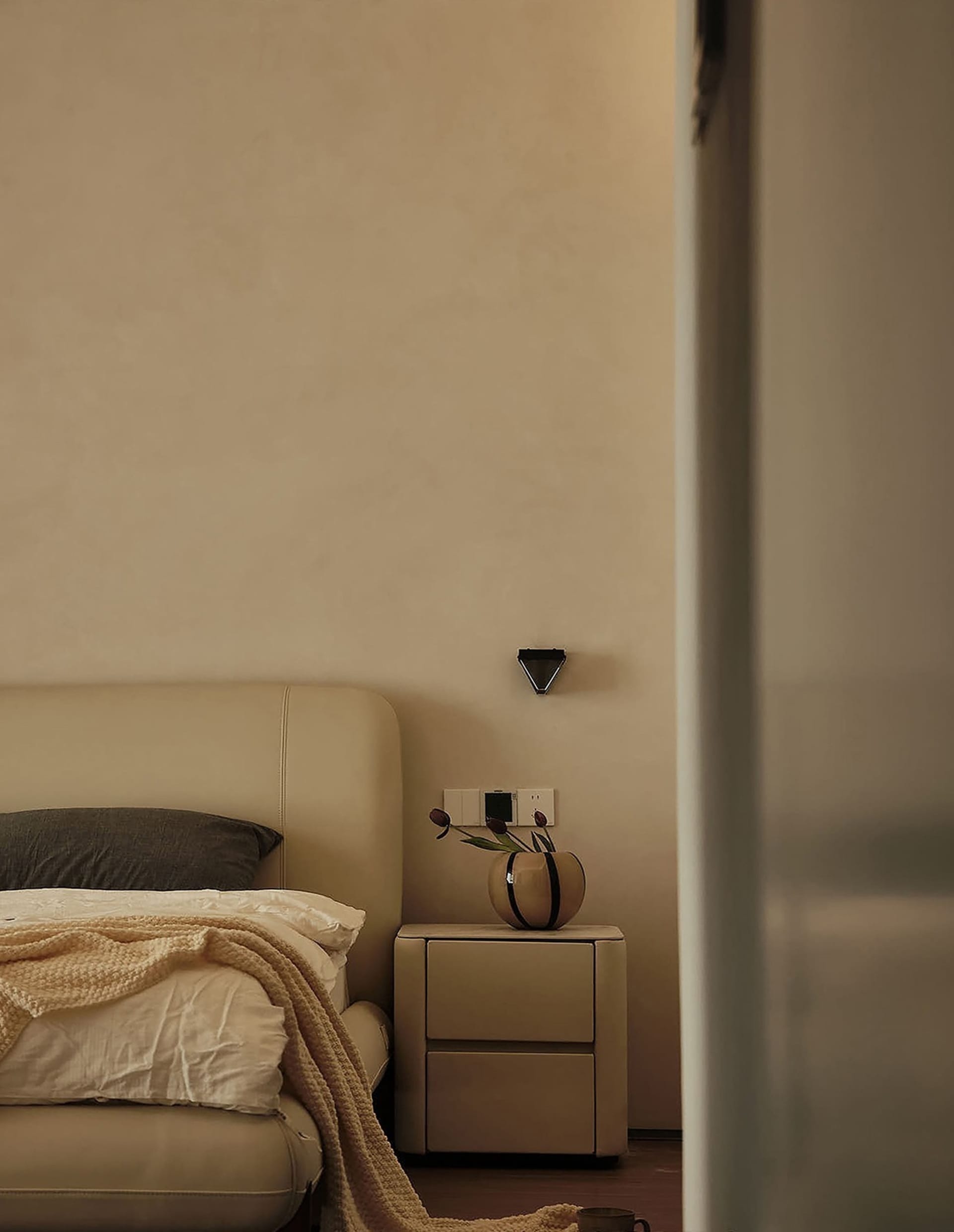 Minimalist bedroom featuring a neutral-toned bedside table with a vase and flowers.