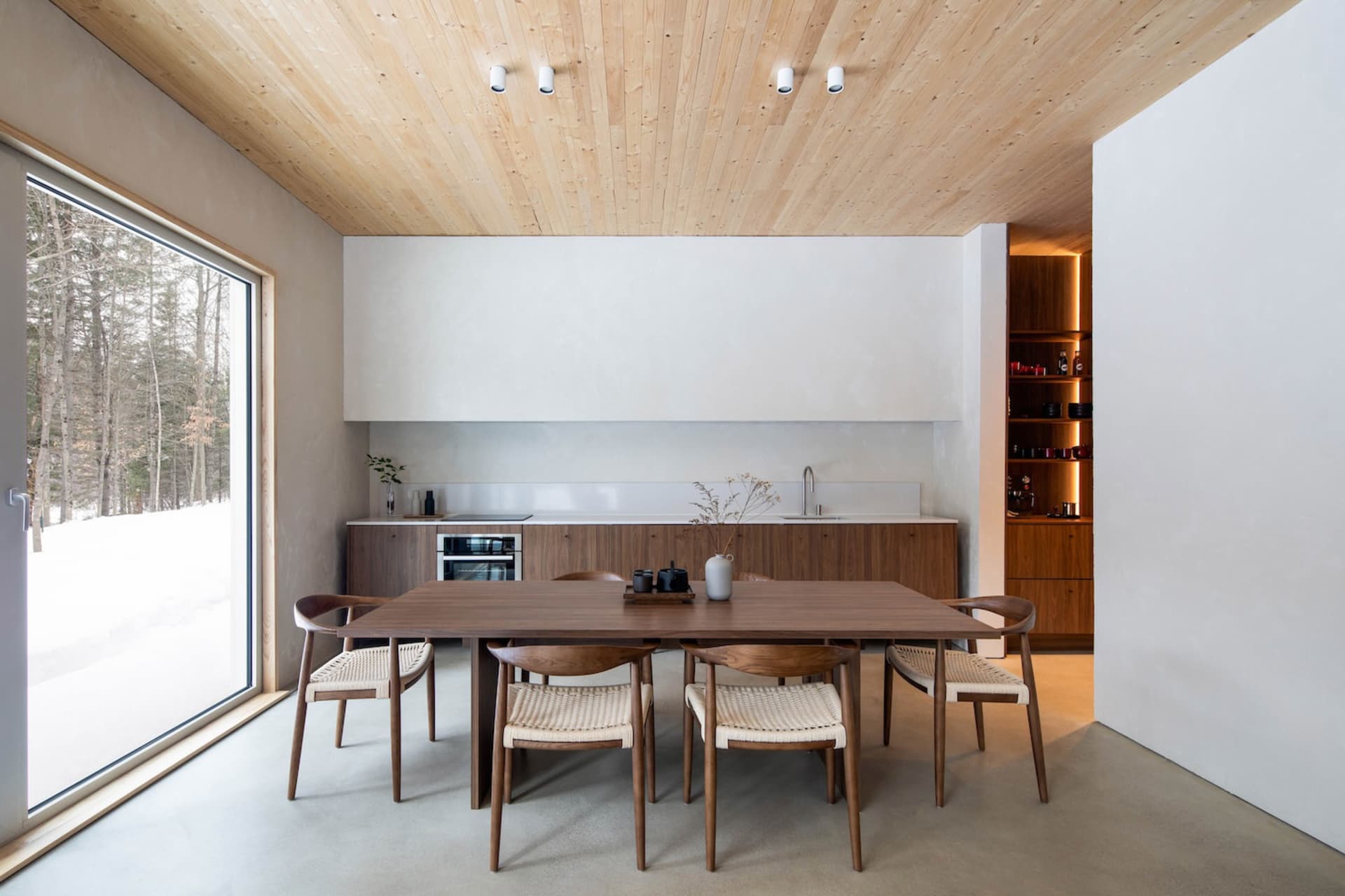 A modern kitchen with wooden cabinetry and a large window showing a snowy landscape.