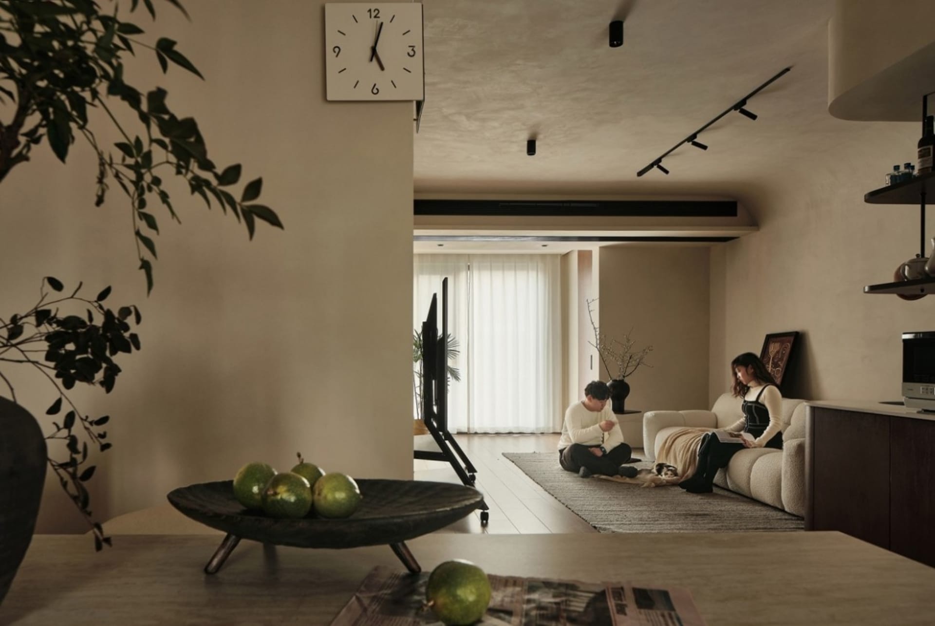 A cozy modern living room featuring a plush sofa, a low coffee table, and a minimalistic clock on the wall.