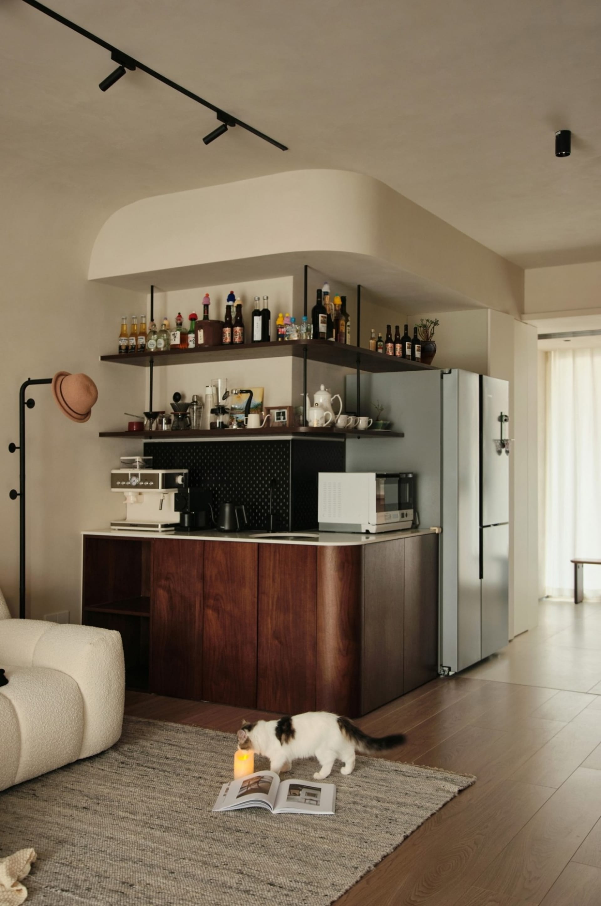 A modern residential kitchen featuring wood and metal materials with a bar counter and a white cat exploring a candle on a ru