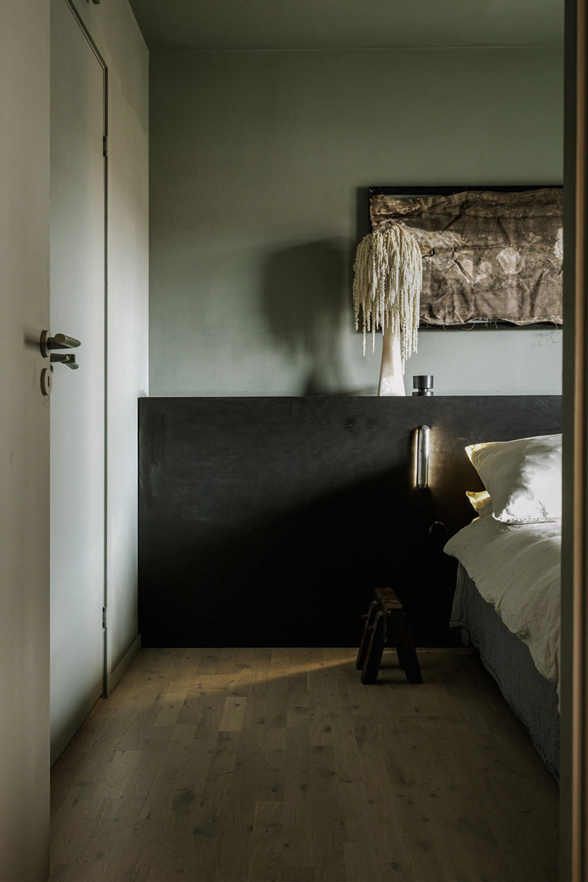 A minimalist bedroom with a black wooden headboard and a white bed, featuring a unique hanging lamp and a textured wall decor