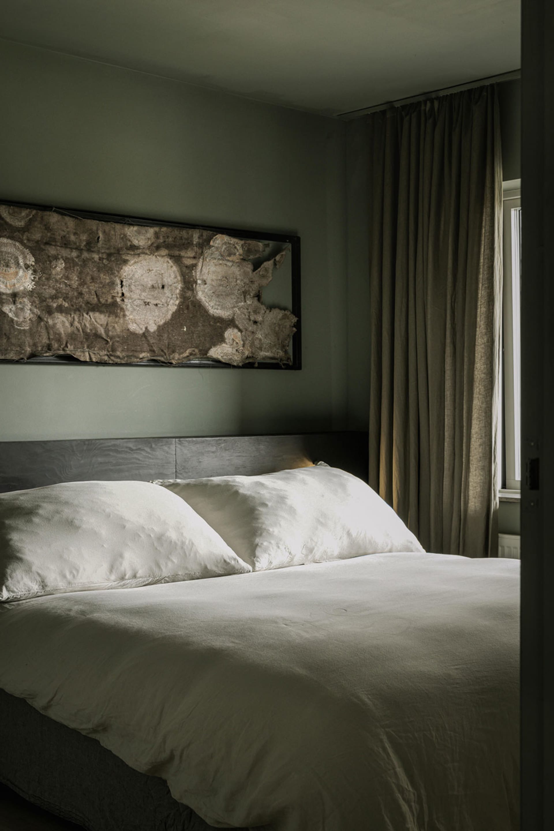 A minimalist bedroom with soft textiles and natural materials, featuring a bed with white bedding and wooden headboard, and a