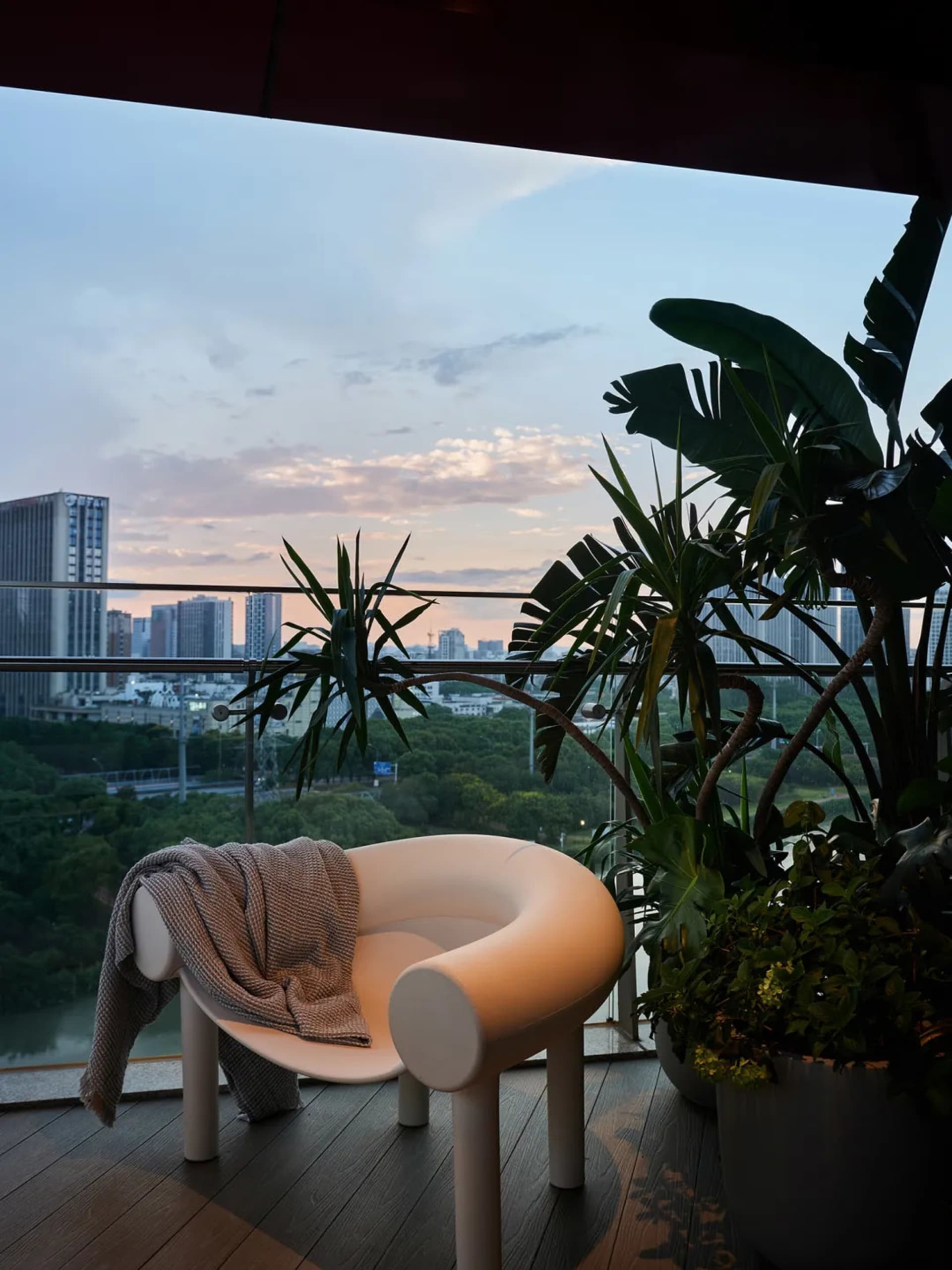 Modern balcony featuring a city view with potted plants and a wooden deck.