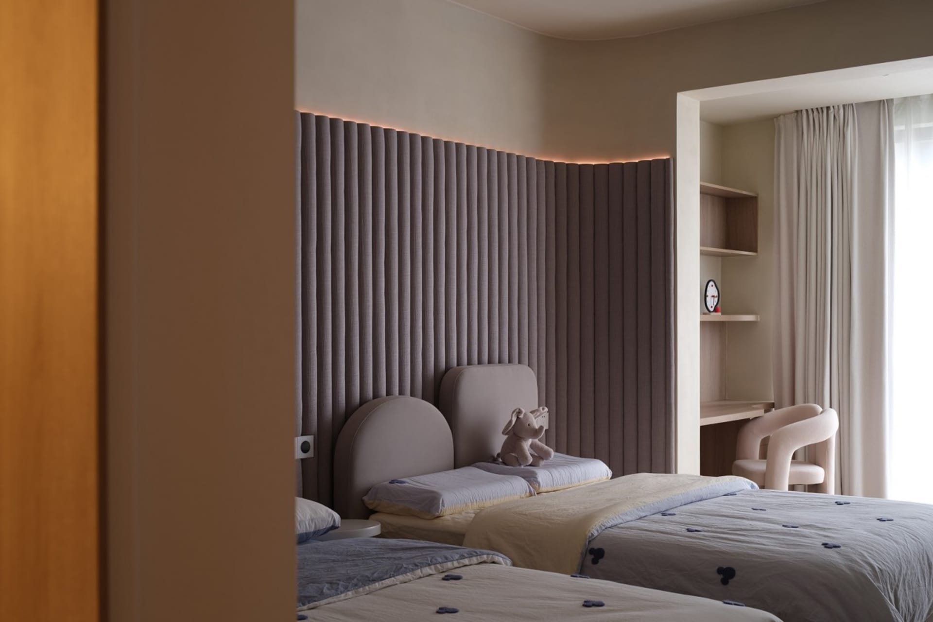 A modern minimalist bedroom with grey curtains, fabric headboards, and light wooden furnishings.